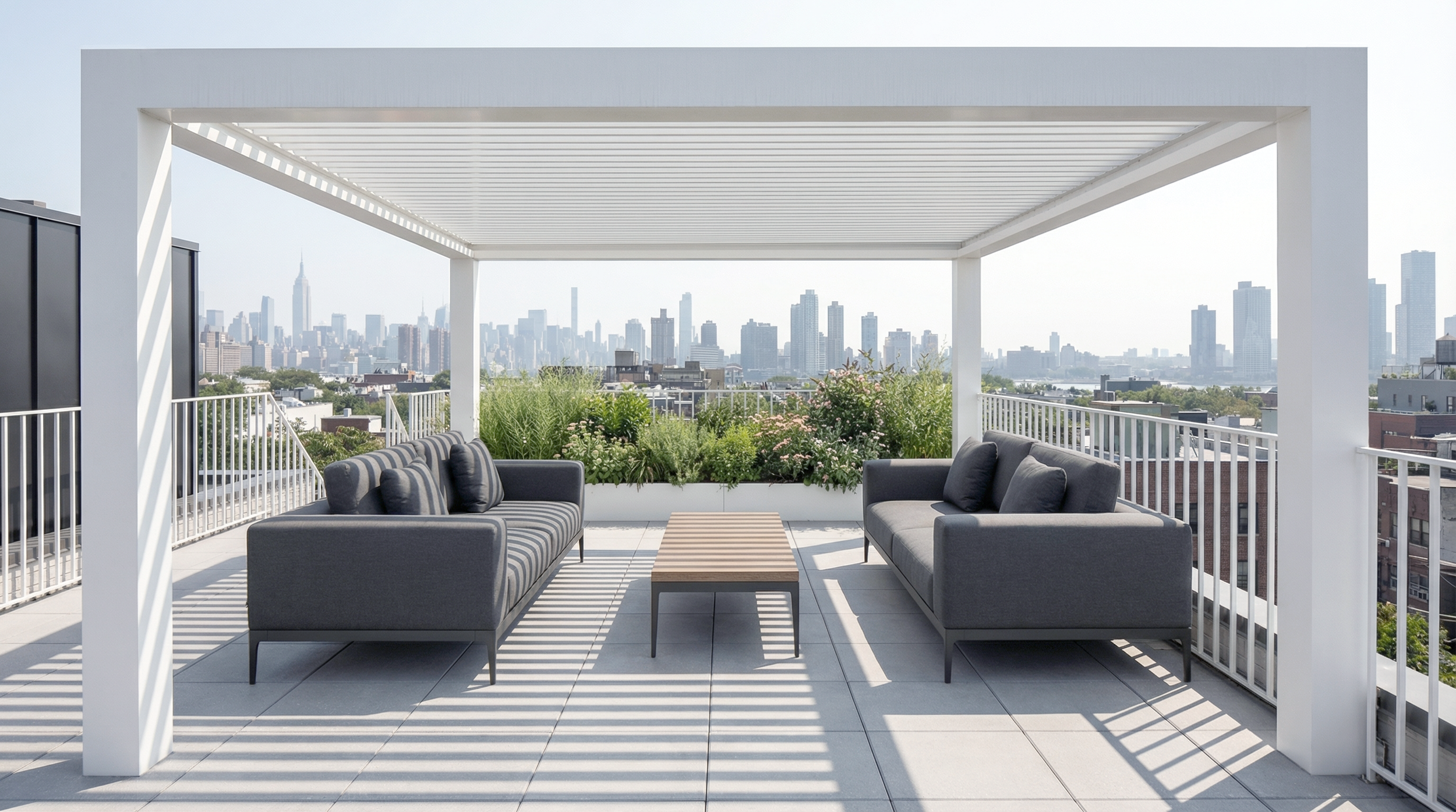 Rooftop terrace with two gray sofas facing each other, a small wooden table between them, potted plants, and a city skyline in the background.