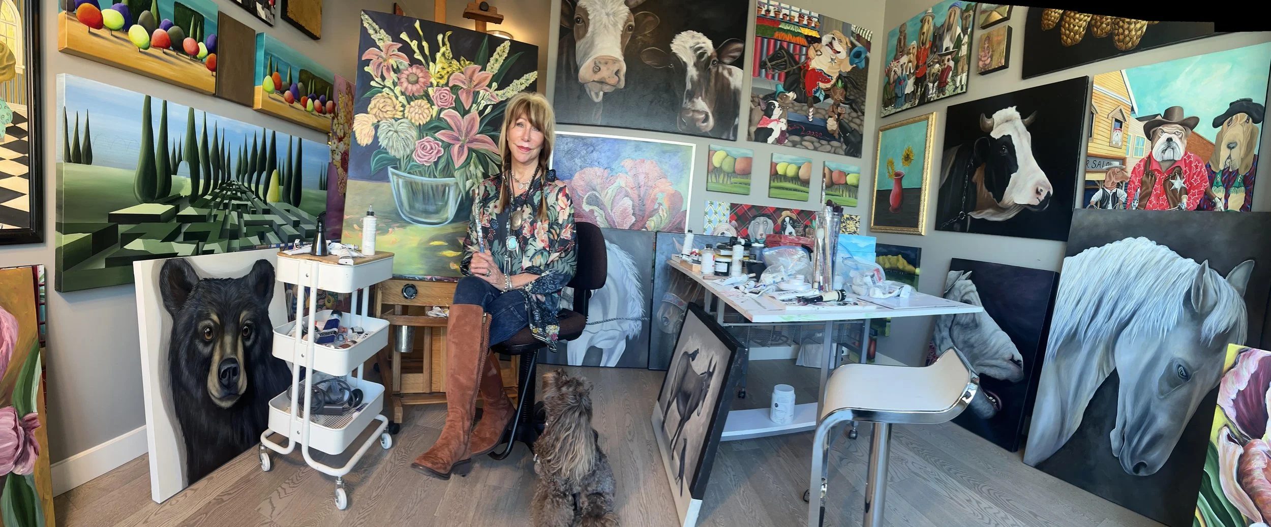 Nyree's studio filled with colourful paintings, including portraits of animals and abstract scenes, and Nyree herself, surrounded by her artwork and her dog.