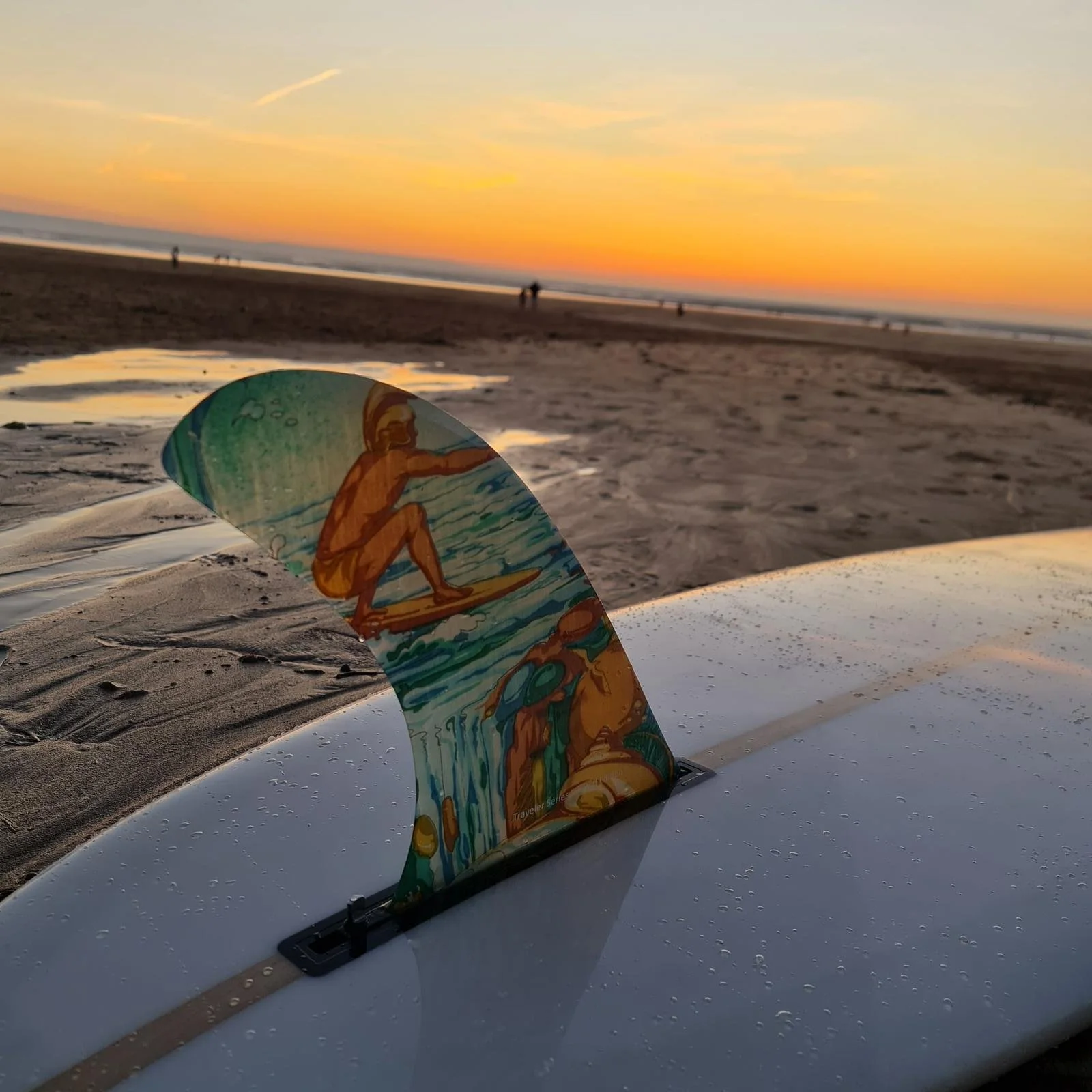 Carl enjoying time at the beach surfing against a beach sunset with a few people walking along the shoreline.