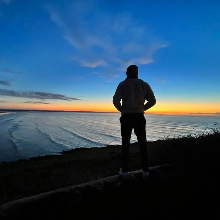 Carl looking at a sunset over the ocean with a partly cloudy sky.