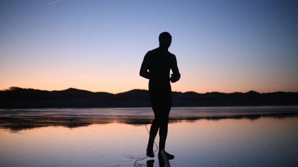 Carl standing on a beach at sunset with calm water.