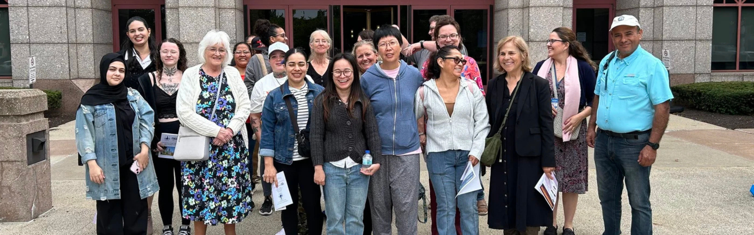 Group of people smiling, gathering in front of a buiilding.