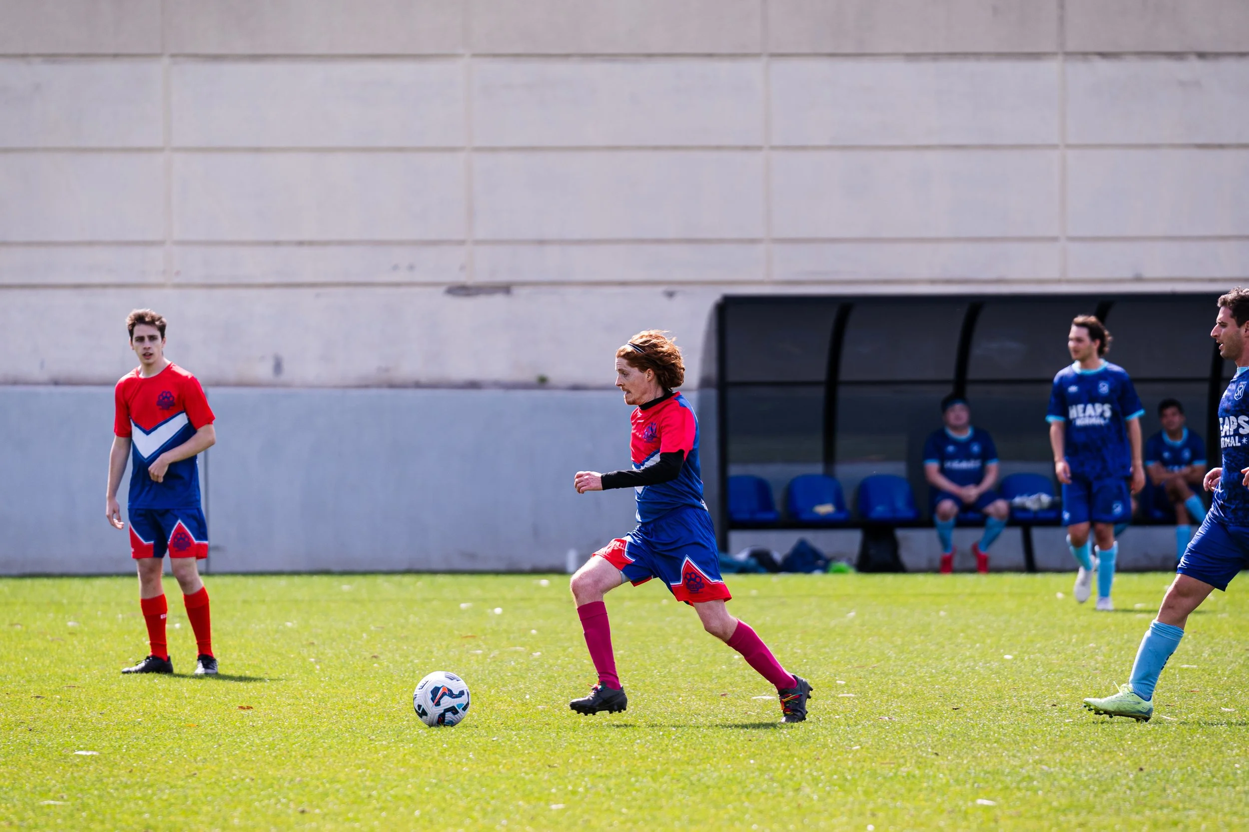 Soccer players on the field, one about to kick the ball, others watching and sitting on the bench.