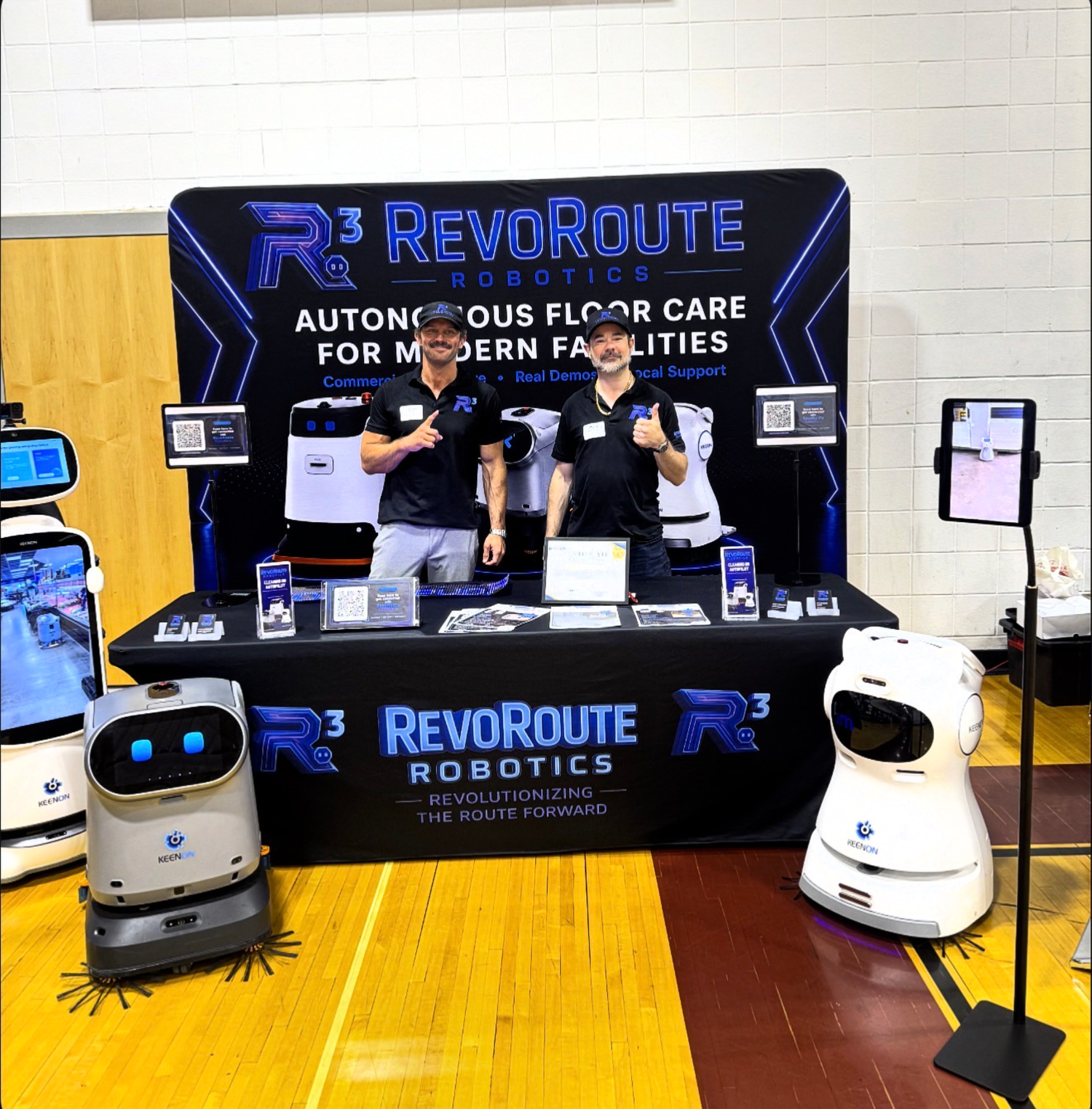 Taylor Buker and Mark Harrington at the RevoRoute Robotics trade show booth with two KEENON robots