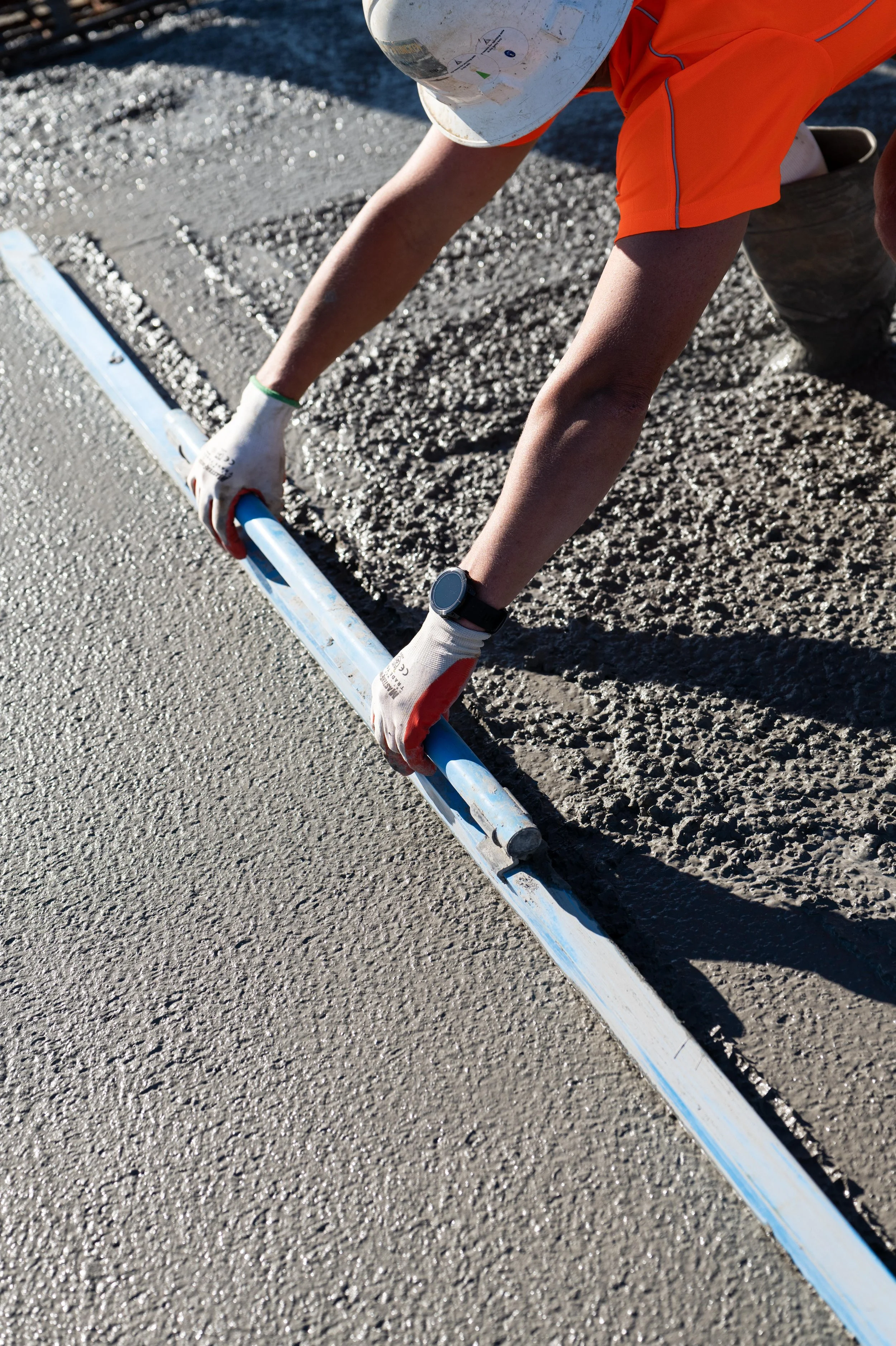 A construction worker smoothing out a freshly poured concrete slab on a sunny day.