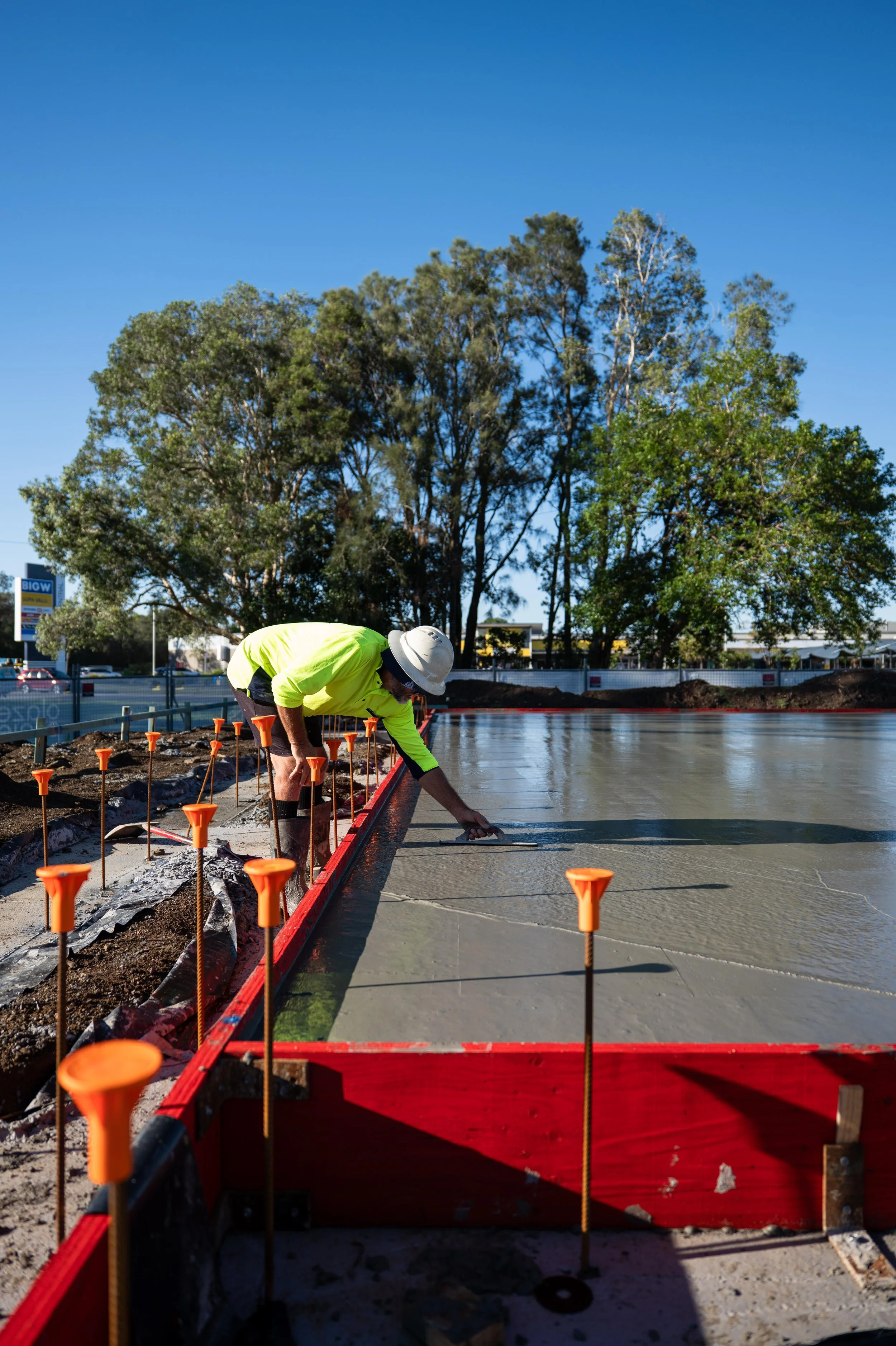 Construction worker smoothing concrete on a building slab on a sunny day with trees in the background.