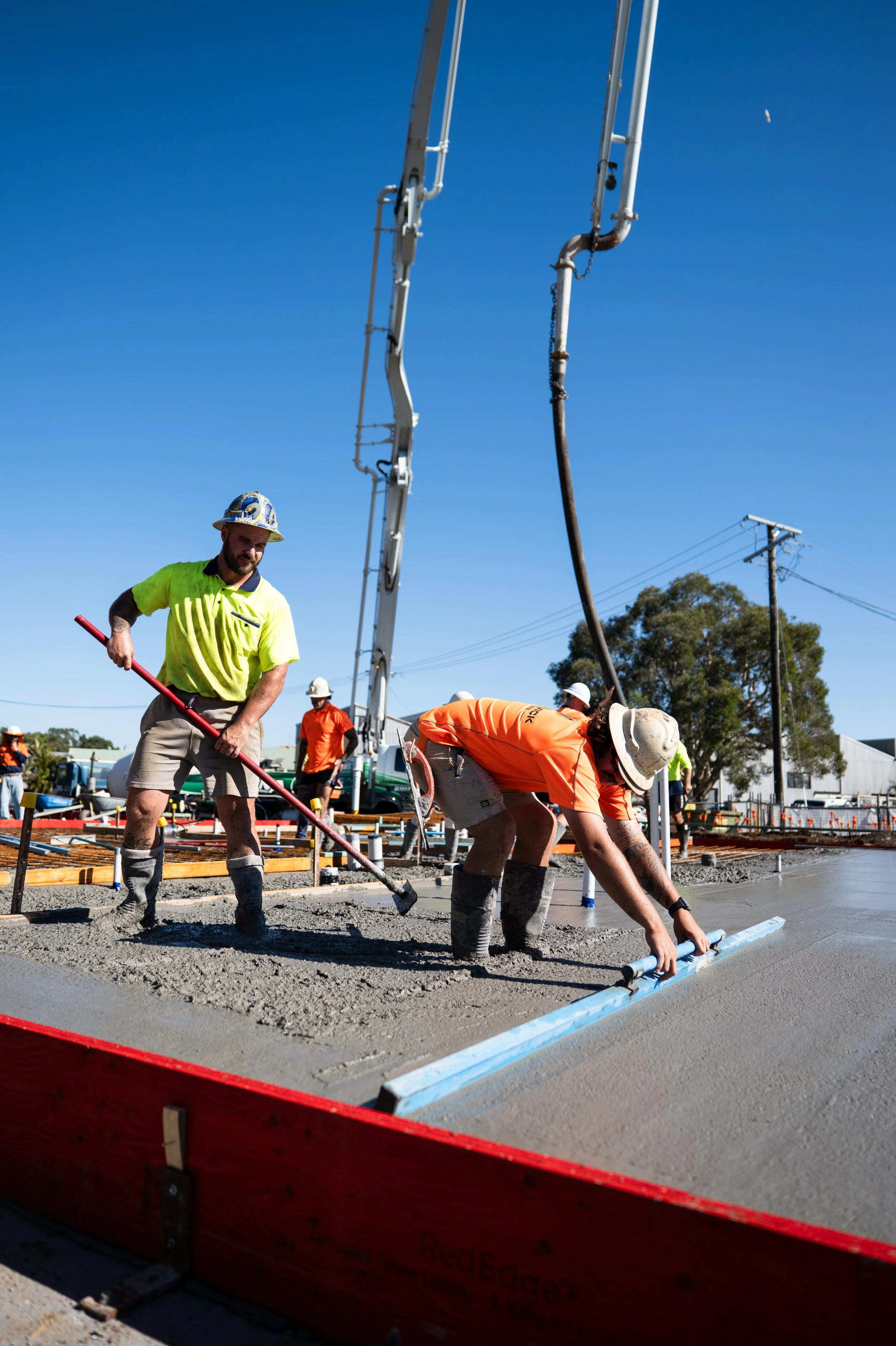 Construction workers pouring and smoothing concrete on a sidewalk or road under a clear blue sky.