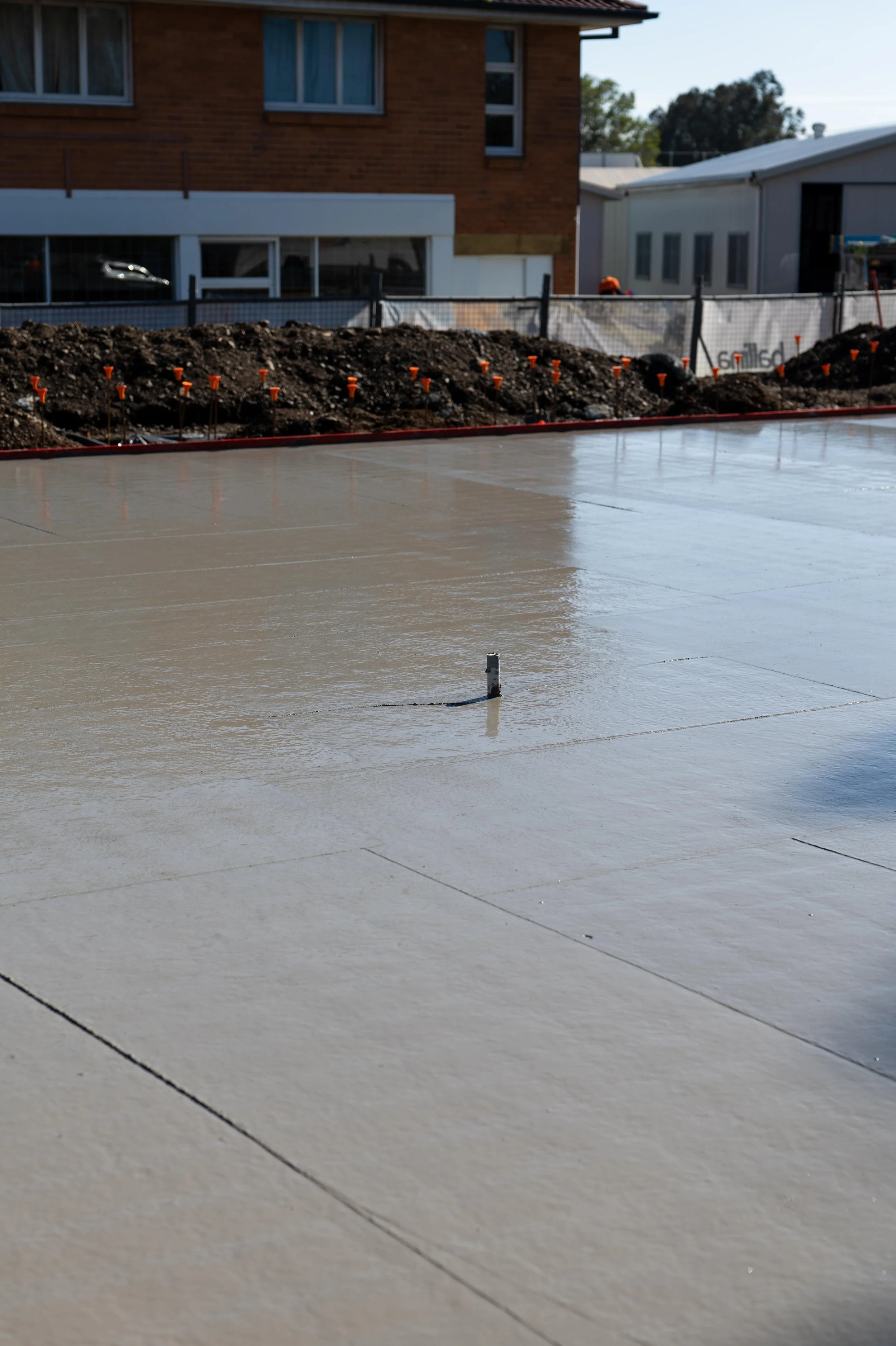 Freshly poured concrete slab on a construction site with a house and other buildings in the background.