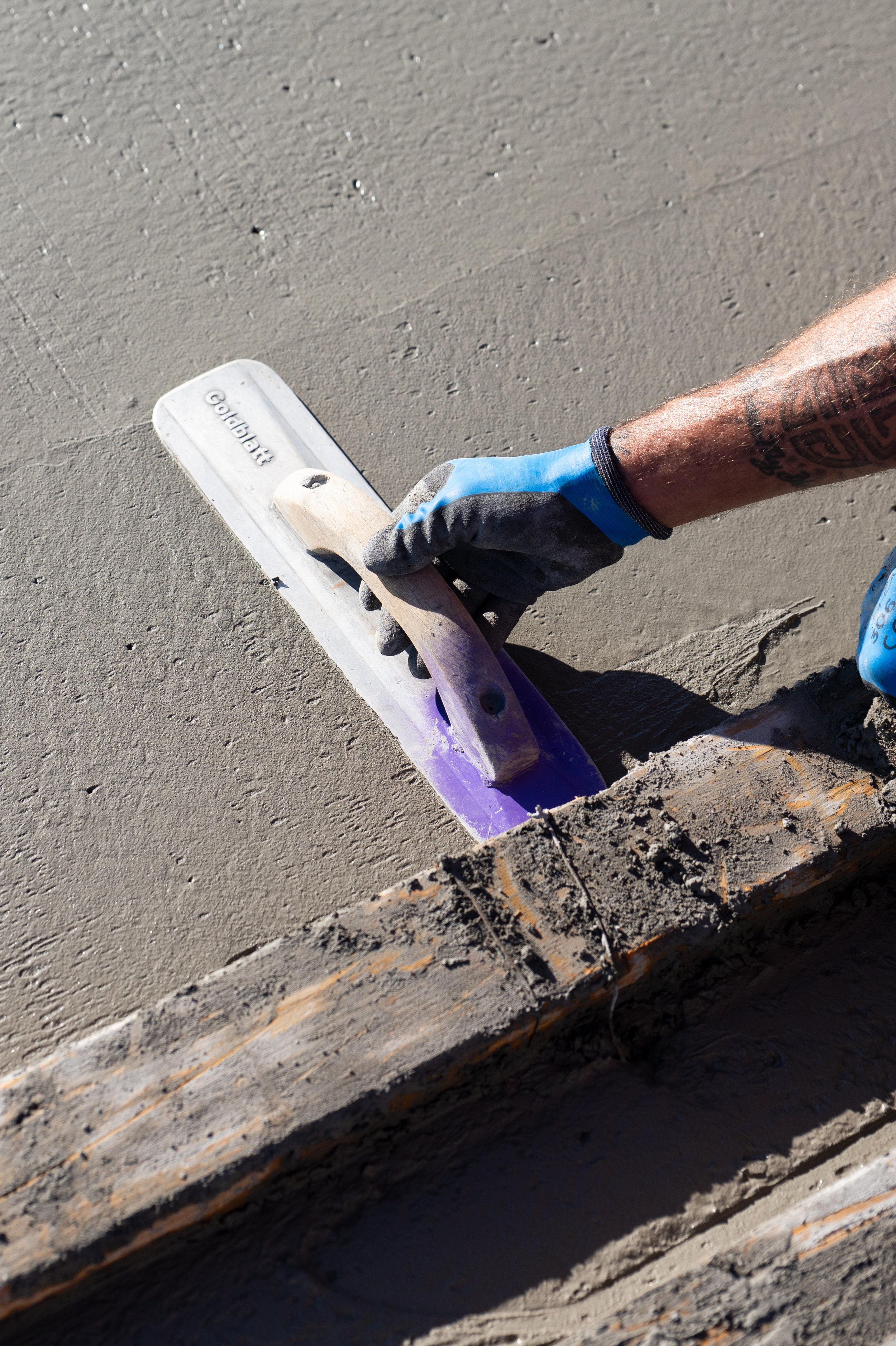 A person smoothing wet concrete with a trowel while wearing a black glove with a blue wristband.