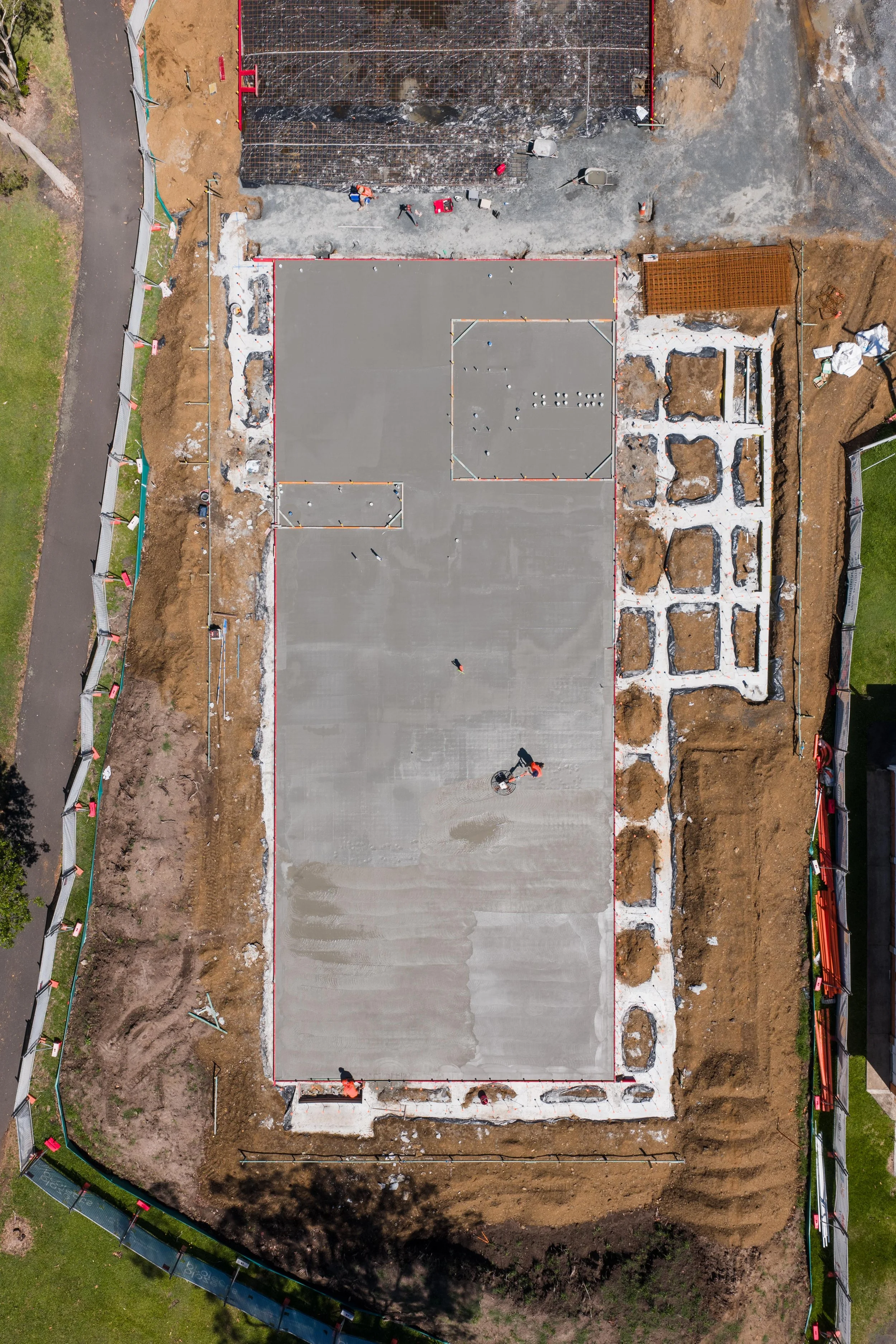Aerial view of a construction site with a concrete foundation, some workers, and surrounding excavation and fencing.