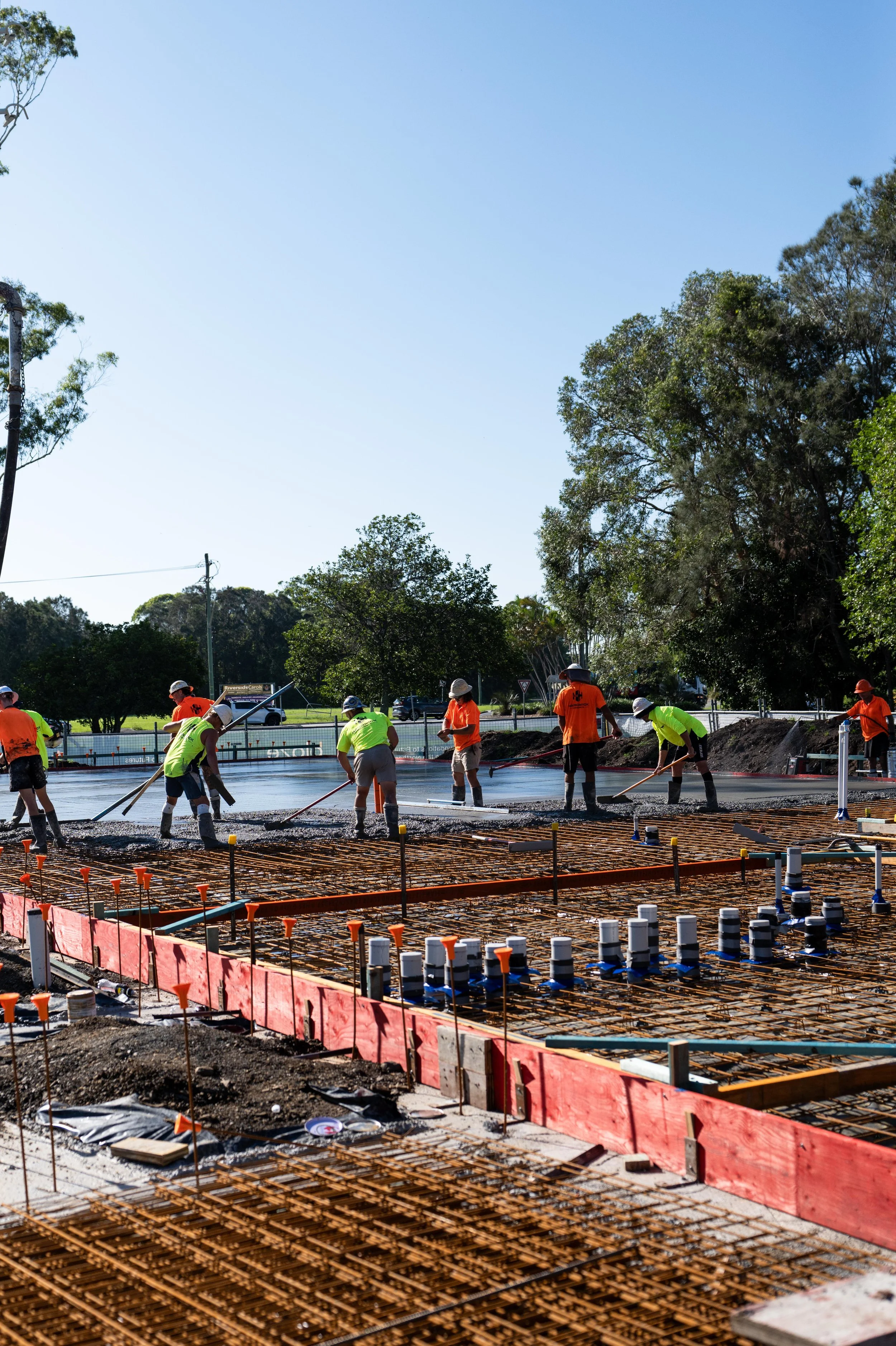 Construction workers pouring and smoothing concrete on a foundation with rebar and formwork.