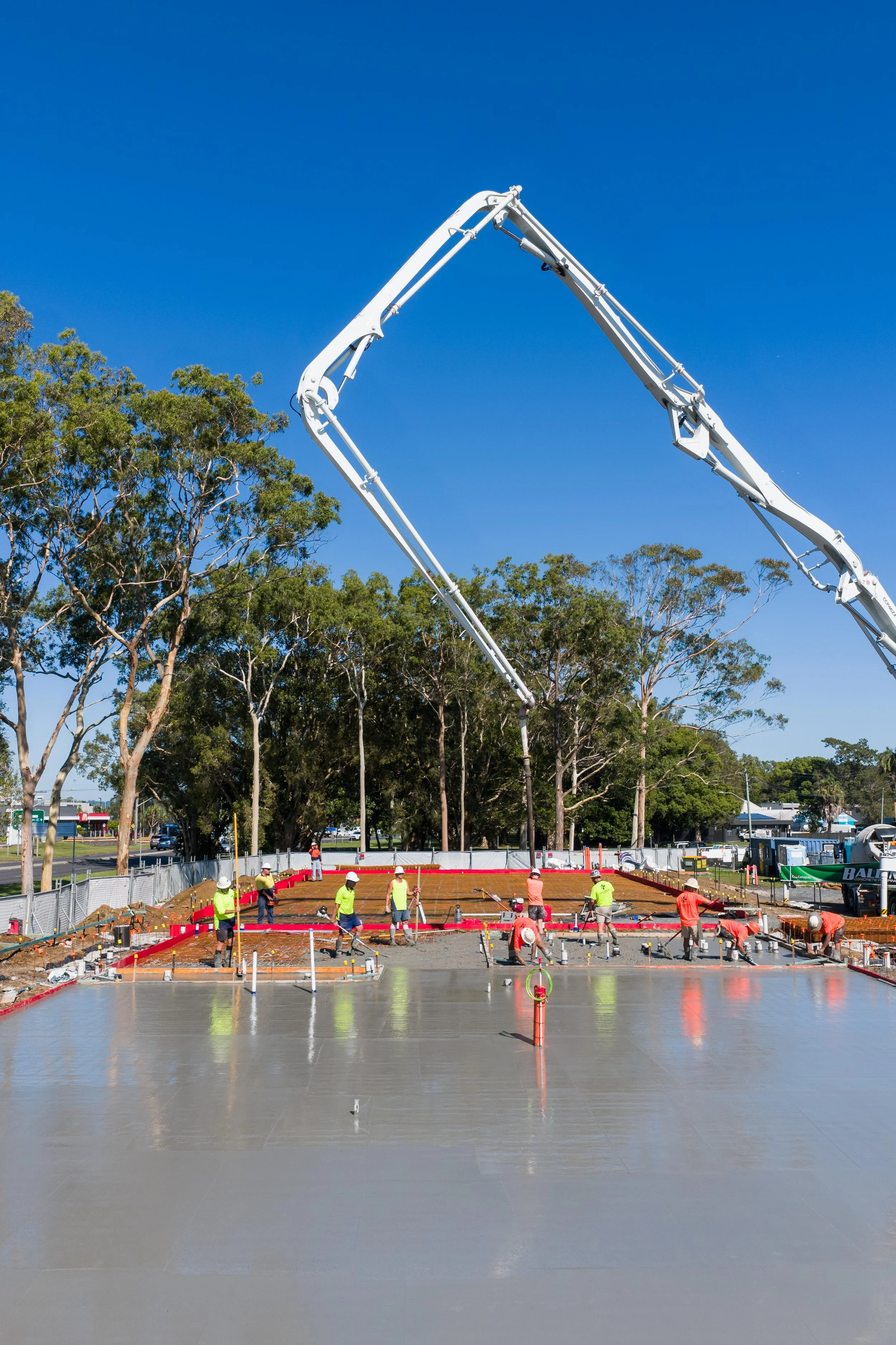 Construction workers pouring and finishing concrete on a building foundation with a concrete pump truck overhead.