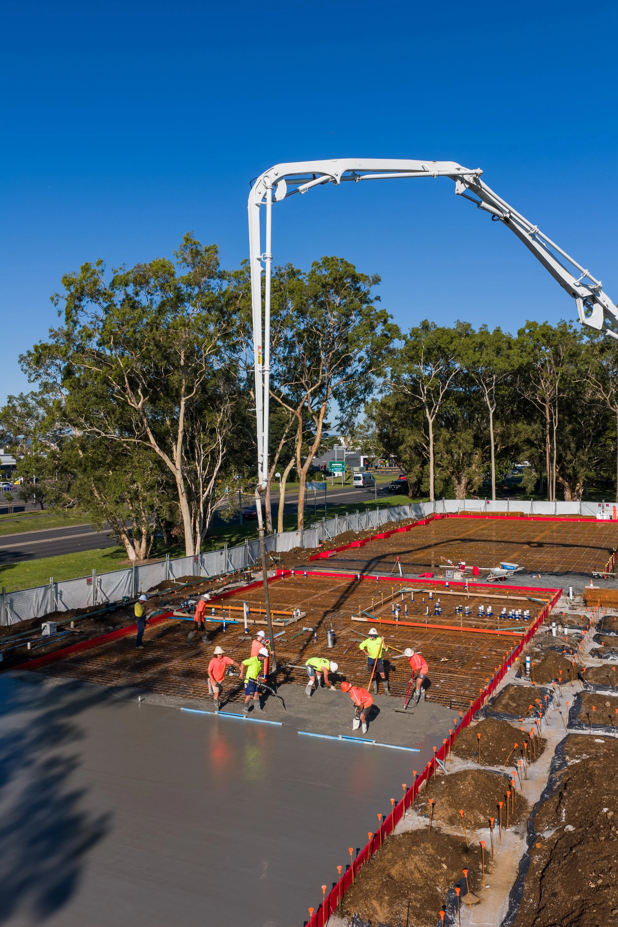 Construction workers pouring concrete to form the foundation of a building with a concrete pump truck overhead.