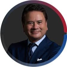 Professional portrait of a man in a dark suit and tie, smiling, with a circular multicolor border