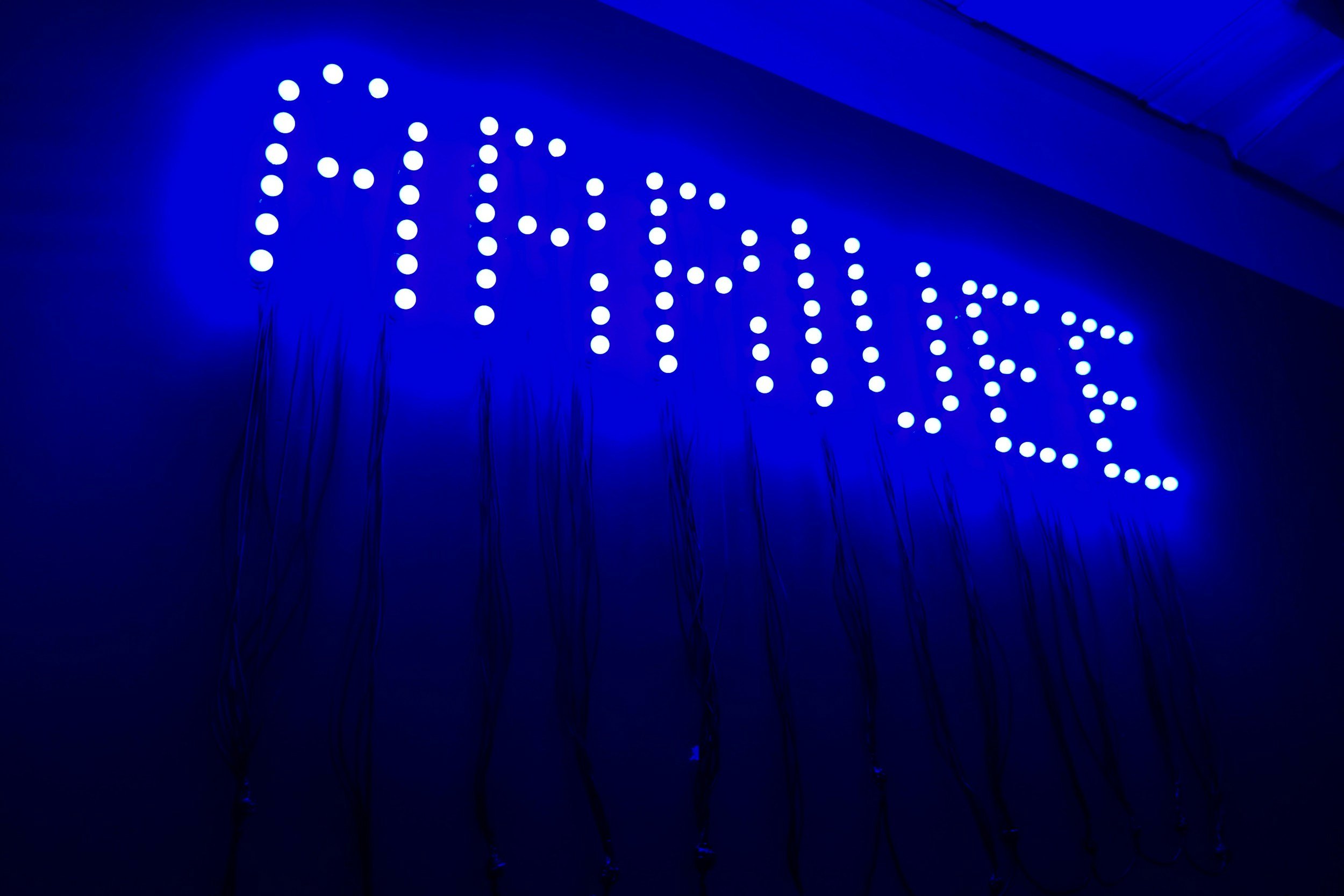 Blue illuminated sign with the word 'Tomorrow' spelled out in white dots on a dark wall.