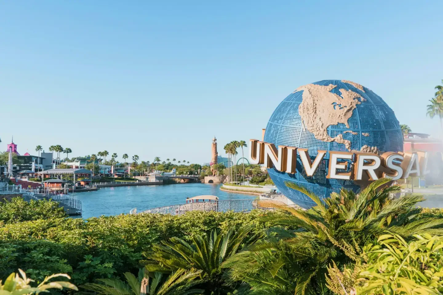 Universal Studios logo featuring a globe with the continents and the word 'Universal' in large letters, set against a theme park with water, palm trees, and buildings.