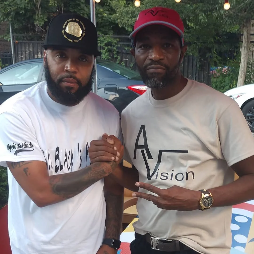 Shyhiem and I standing outside, engaging in a handshake and hand gesture, with cars and greenery in the background.