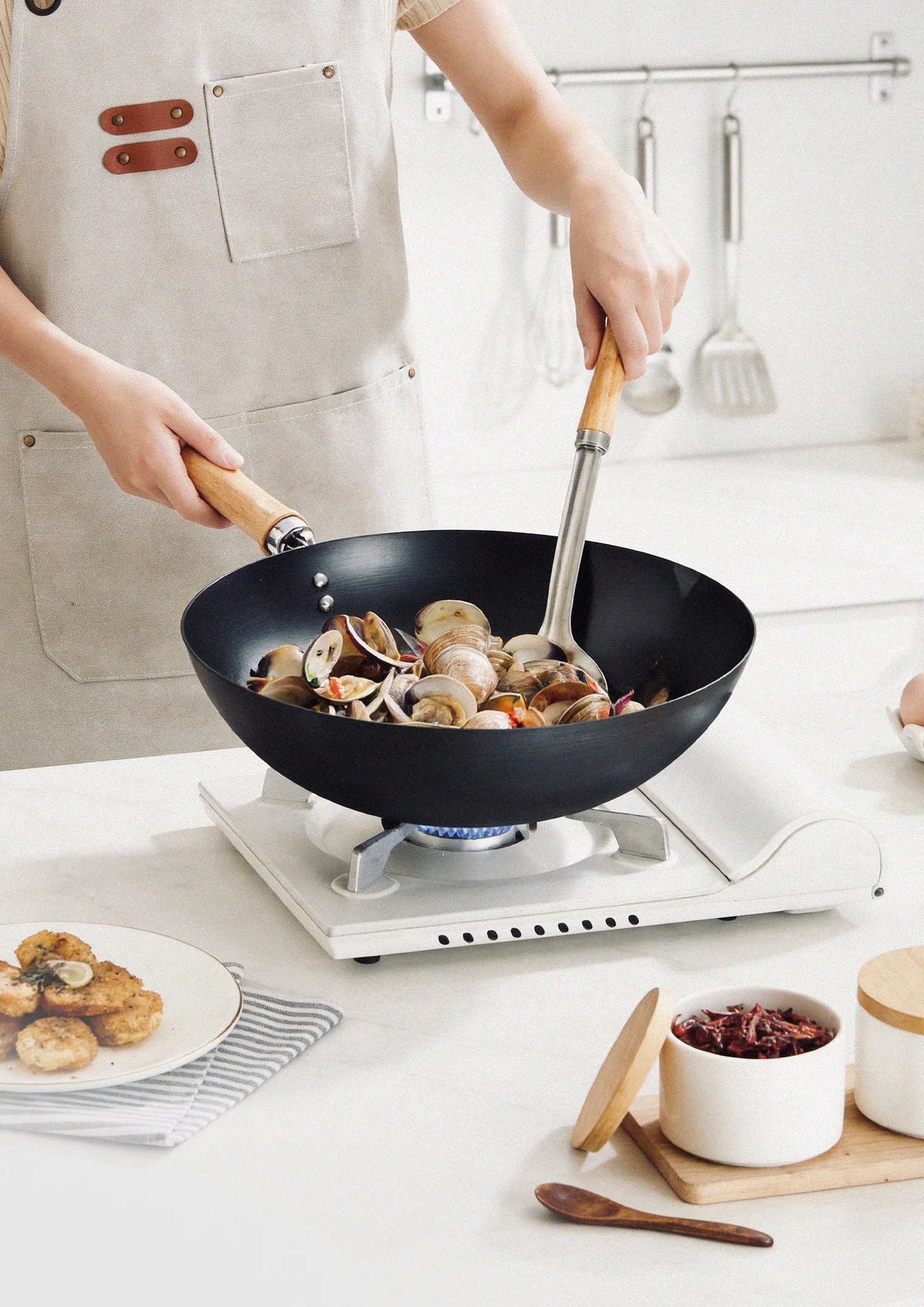 Person cooking clams in a black frying pan on a white stove.