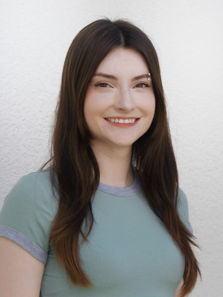 Smiling young woman with long dark hair in front of a light-colored textured wall.