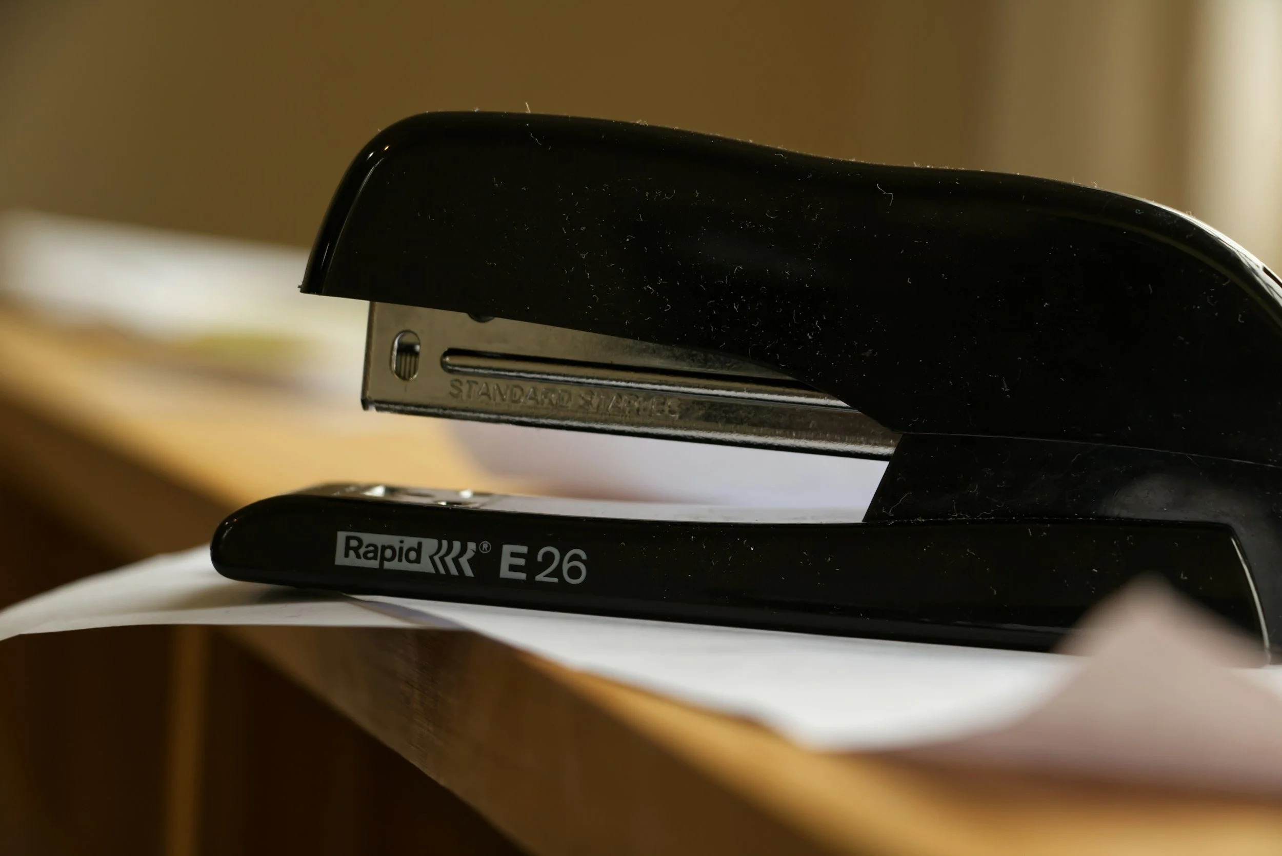 Close-up of a black stapler on a wooden surface with paper underneath.