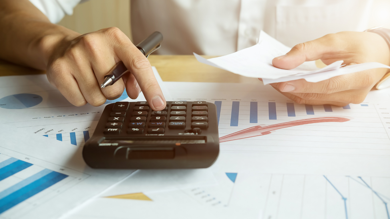Person using a calculator with financial charts and documents on the table.