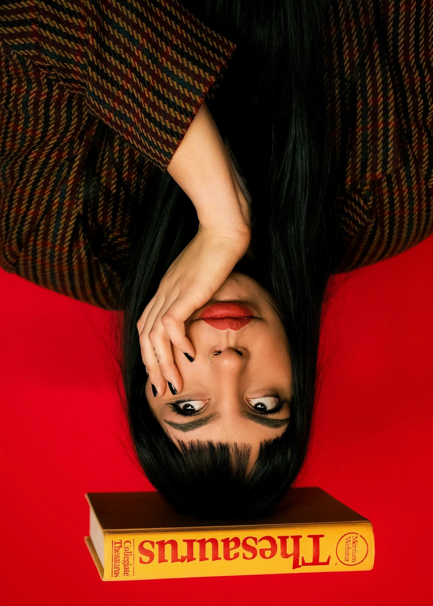A woman with black hair and makeup rests her face on her hand next to a yellow book titled 'Terrorsaurus' against a red background.