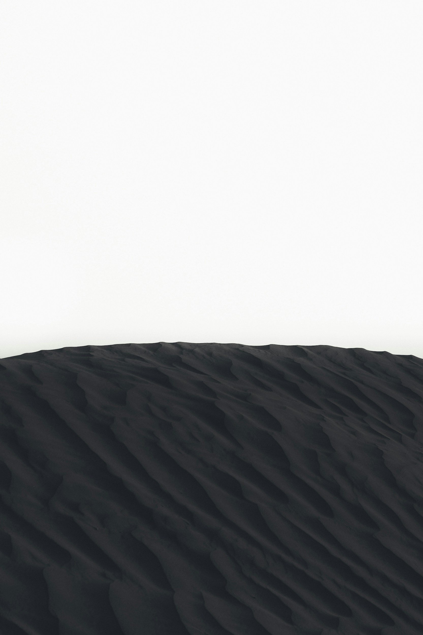 Close-up of dark sand dunes with textured ridges, against a blank white sky.