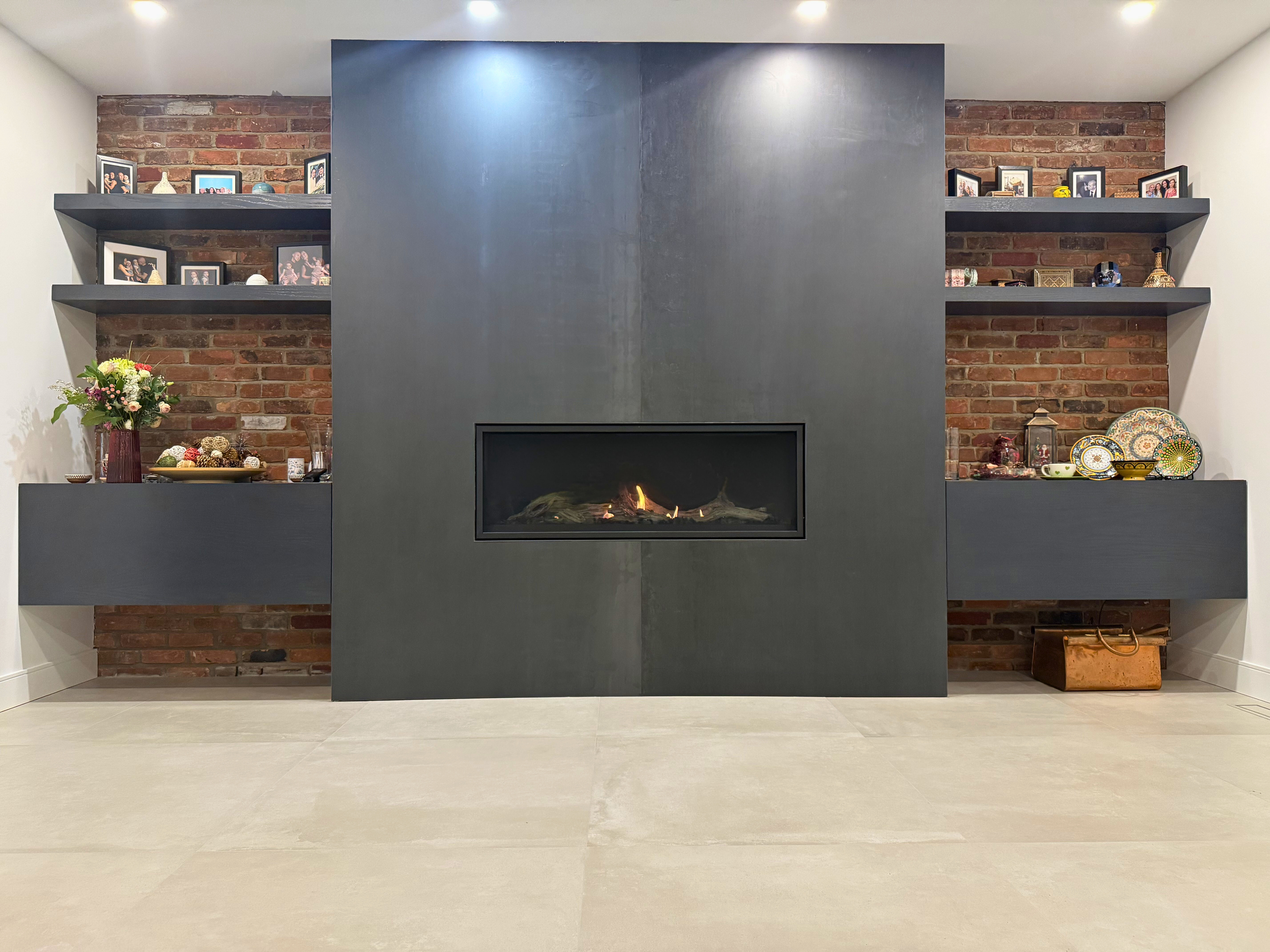 Beaconsfield Residence — Full Home Renovation | Dining room centered around a modern fireplace wrapped in two extra-large black ceramic tiles, set against a contrasting brick wall with custom-built shelving in this West Island Montreal home.
