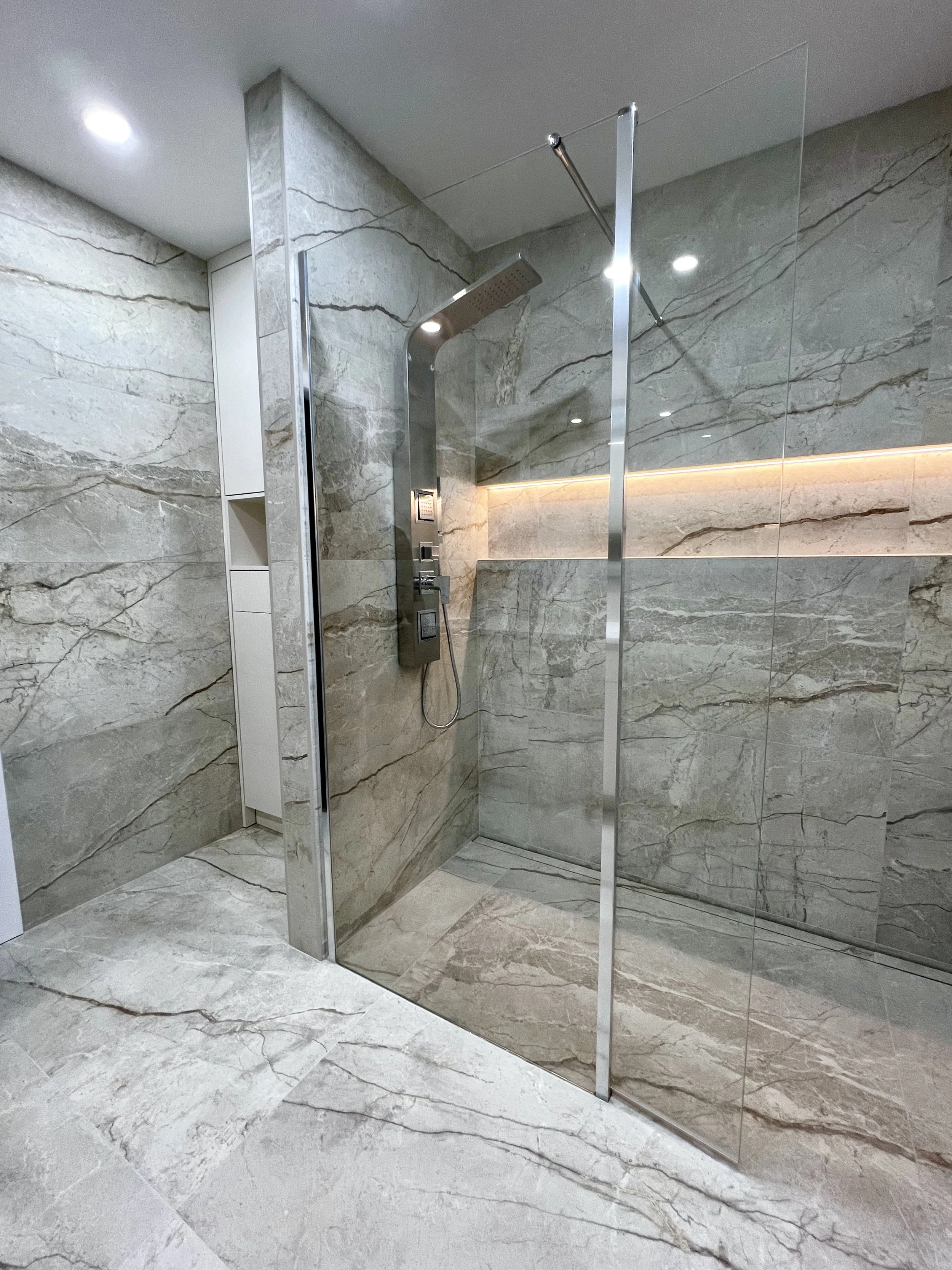 Complete master bathroom transformation in a Beaconsfield residence, West Island Montreal, featuring a tub-to-shower conversion, a spacious walk-in shower with elegant veined ceramic tiles, and custom-built bathroom cabinetry