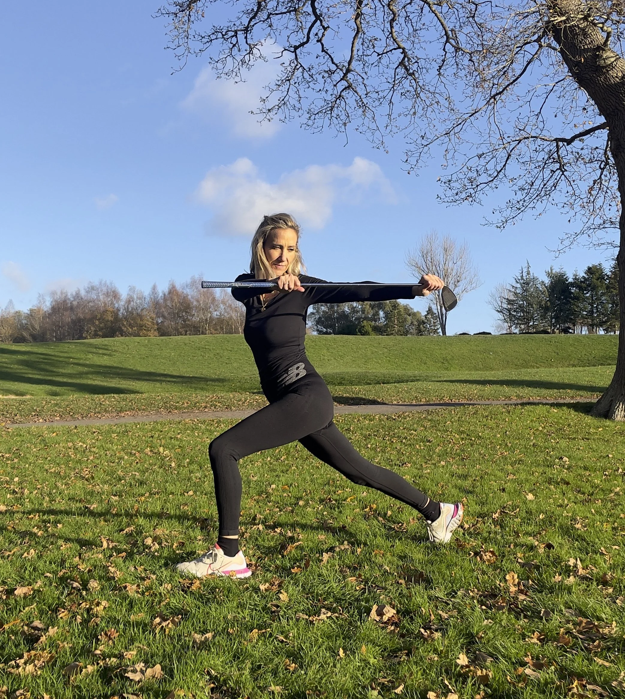Hellen Barlow, Yoga for Golfers Coach, showing a high lunge twist yoga move, while holding a golf club