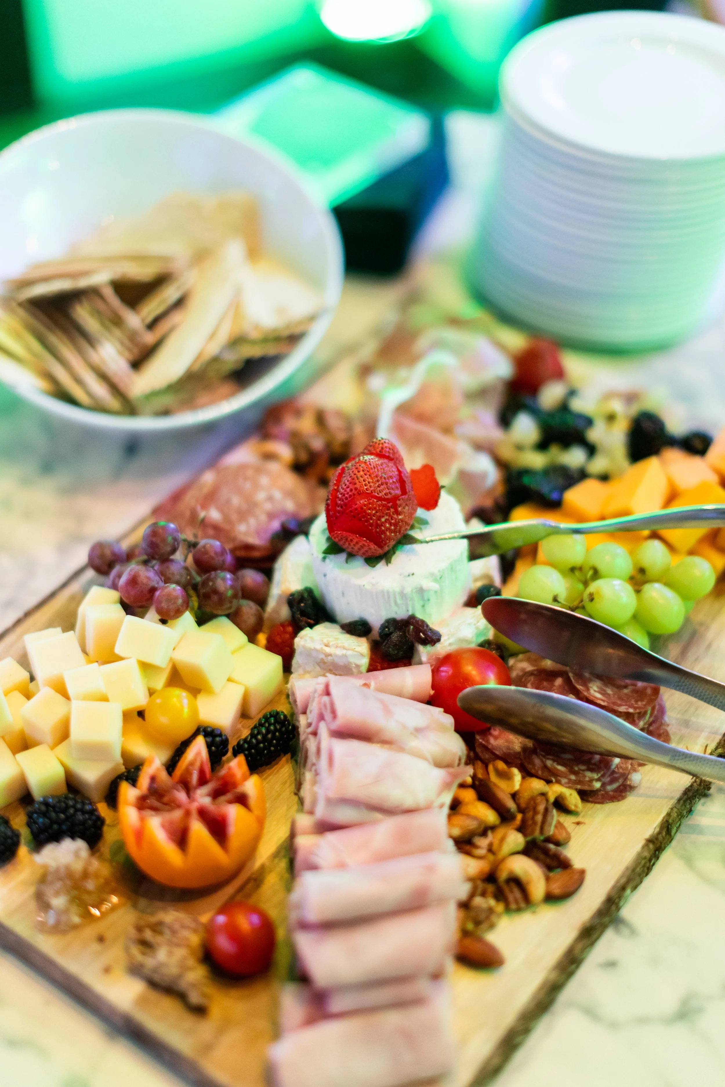 A cheese and charcuterie platter with grapes, berries, cheese, meats, and a small bowl of crackers.