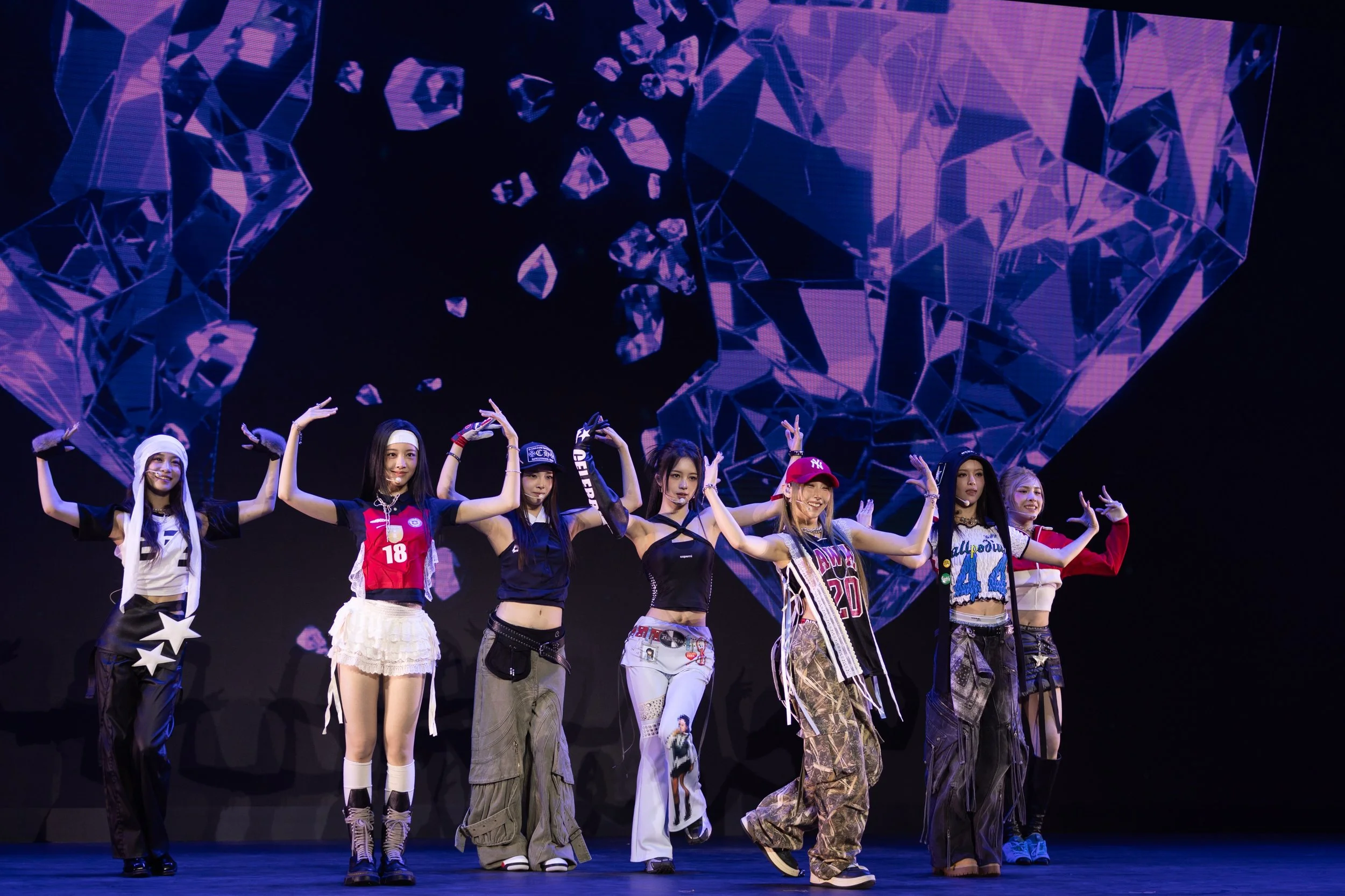 Six young women performing on stage with a digital heart-shaped backdrop.