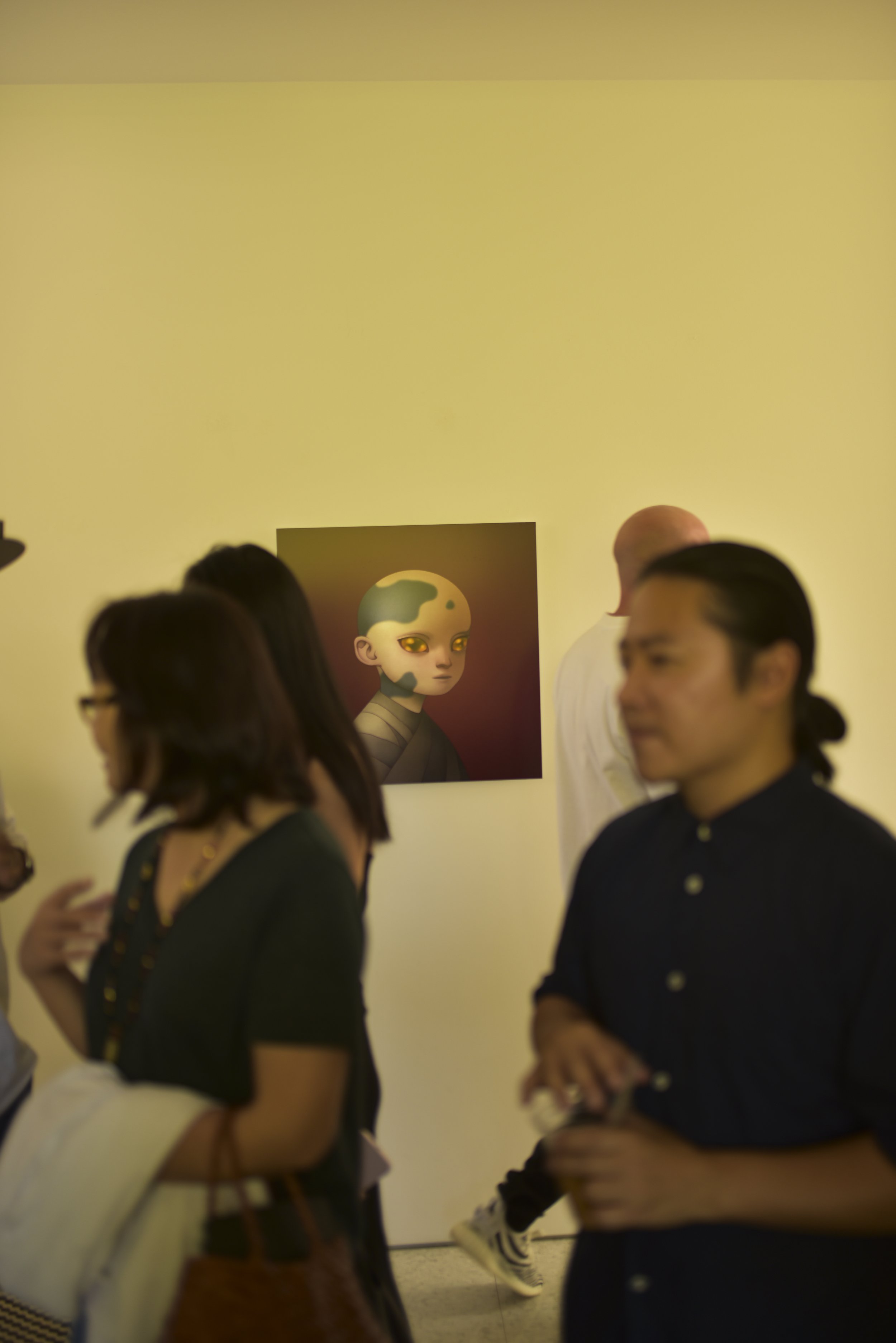 People attending an art exhibition with a digital art portrait of an animated character with green skin, gold eyes, and a striped shirt displayed on the wall.