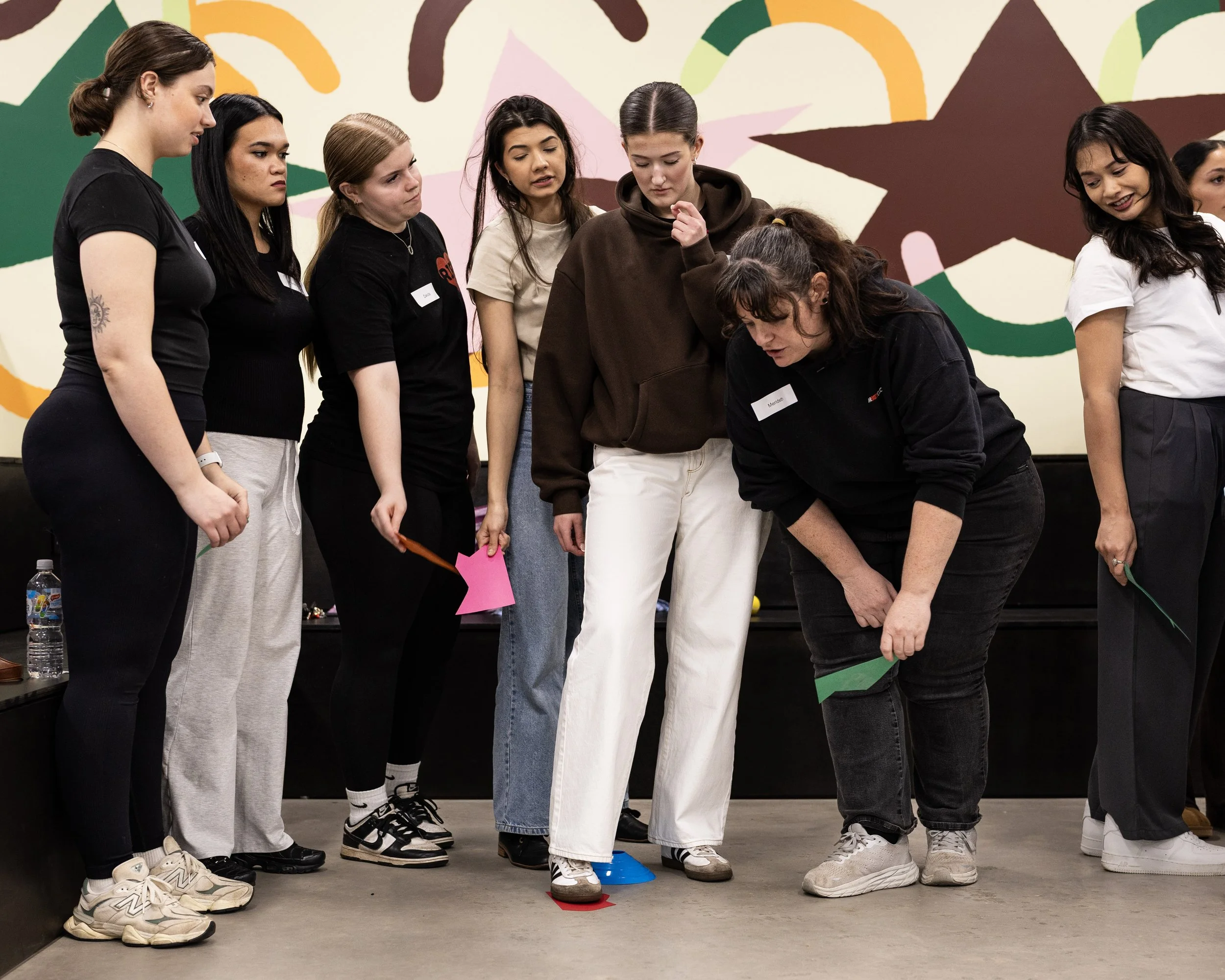 Group of young women standing in a row, participating in a team-building activity involving coloured cones on the floor,  provided by Field9 team building experiences in Adelaide.