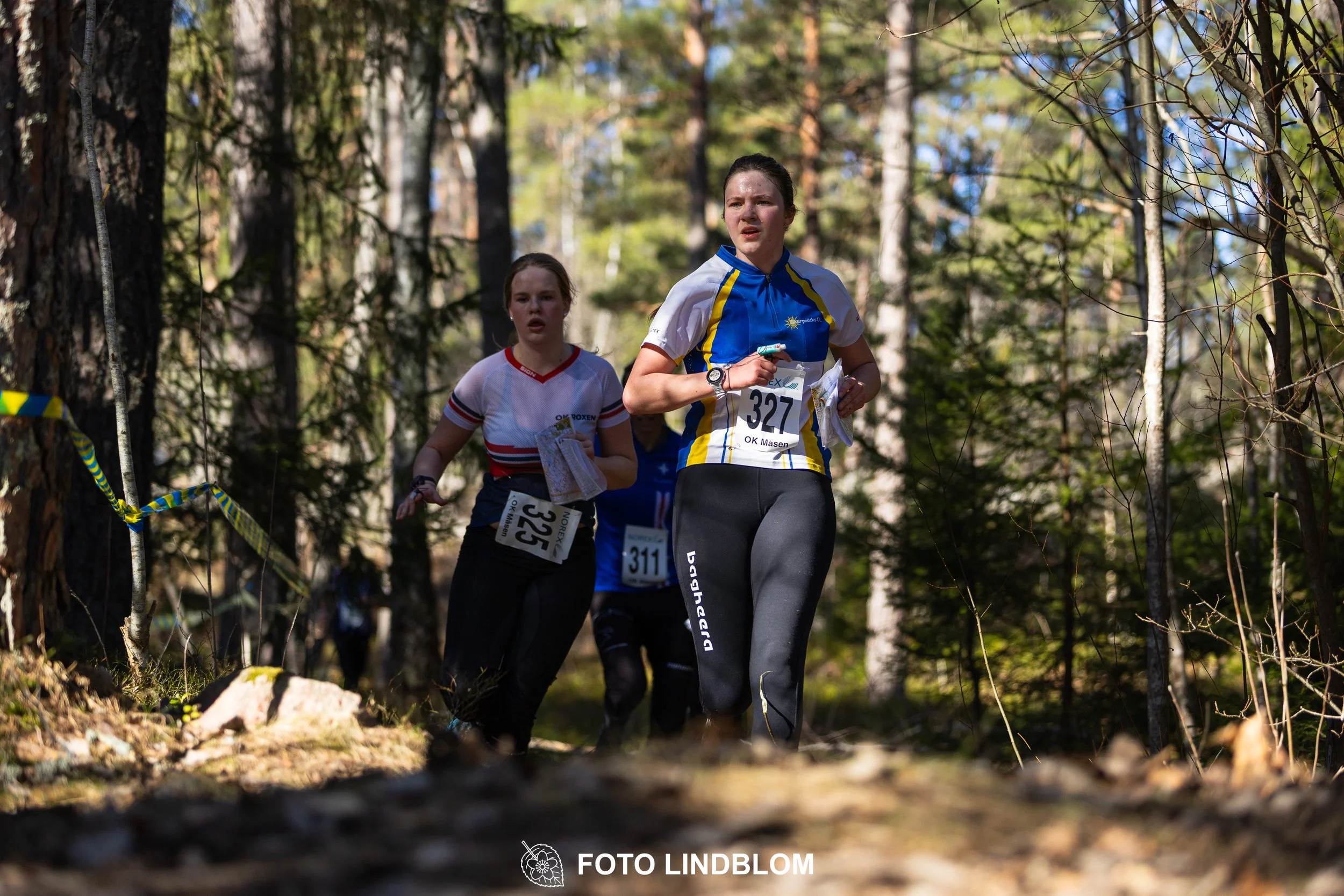 Swedish orienteering relay event Måsenstafetten 2026, with teams racing through forest terrain, captured by Foto Lindblom.