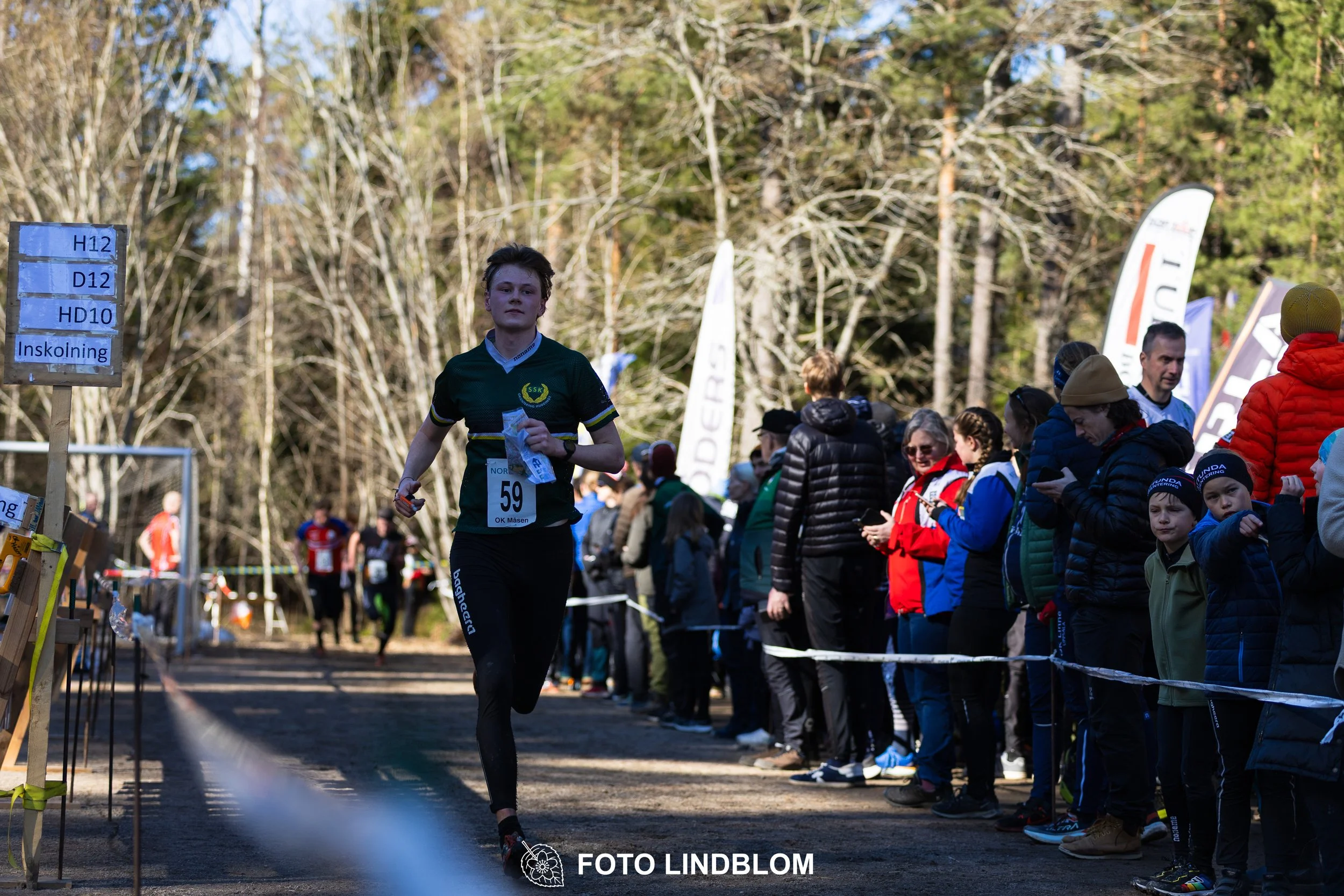 Swedish orienteering relay event Måsenstafetten 2026, with teams racing through forest terrain, captured by Foto Lindblom.