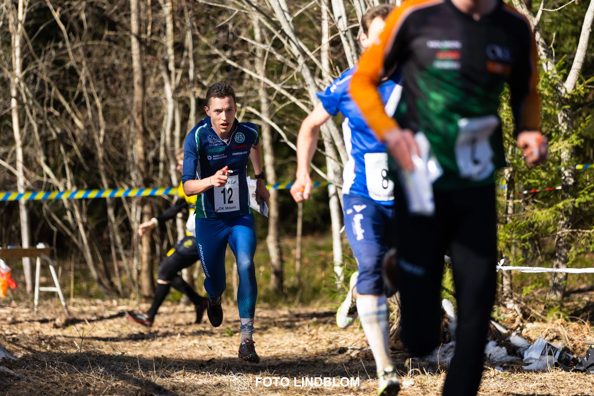 Image from Måsenstafetten 2026 showing orienteering relay teams competing in Swedish forest terrain, taken by Foto Lindblom.
