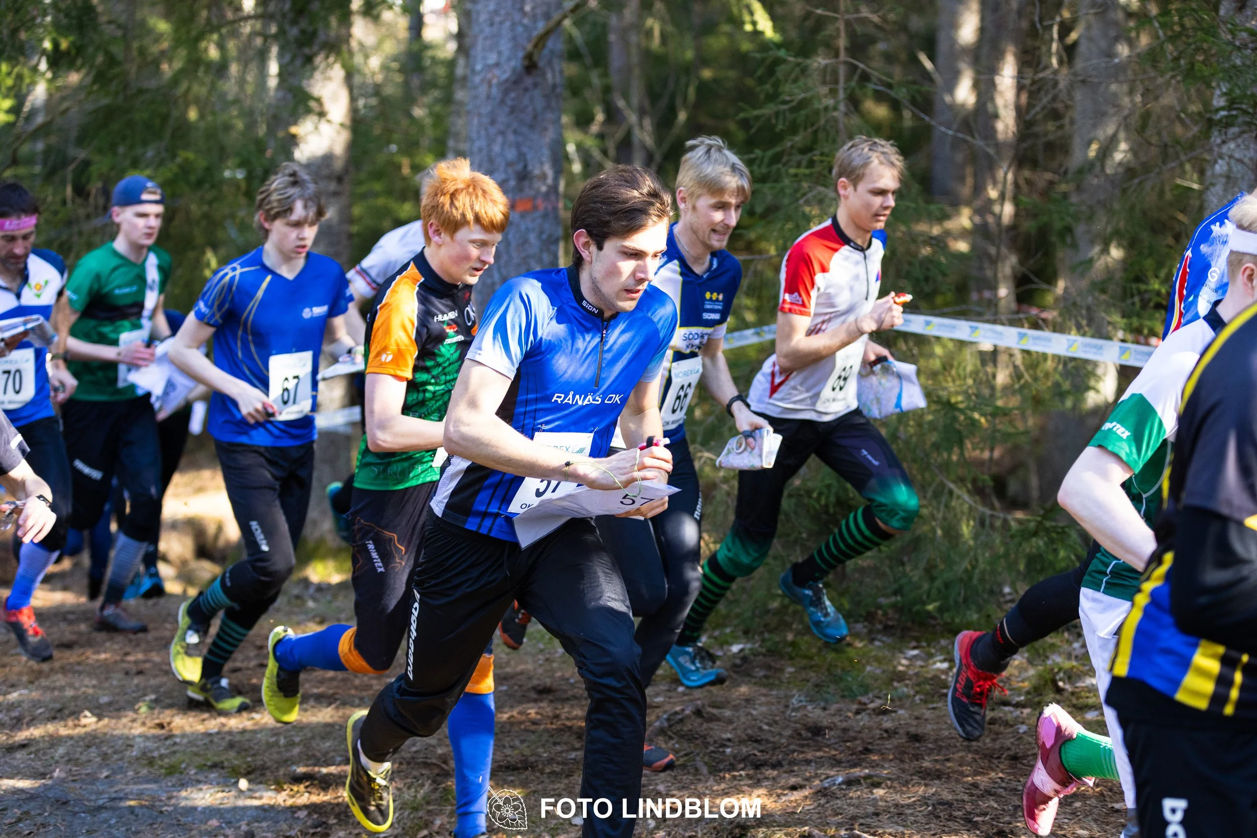 Image from Måsenstafetten 2026 showing orienteering relay teams competing in Swedish forest terrain, taken by Foto Lindblom.