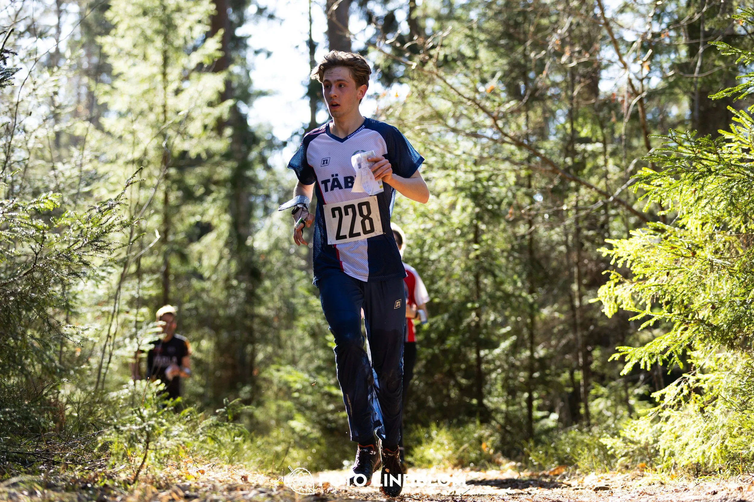 Image from Nyköpingsorienteringen 2026 showing competitors navigating forest terrain, taken by Foto Lindblom.