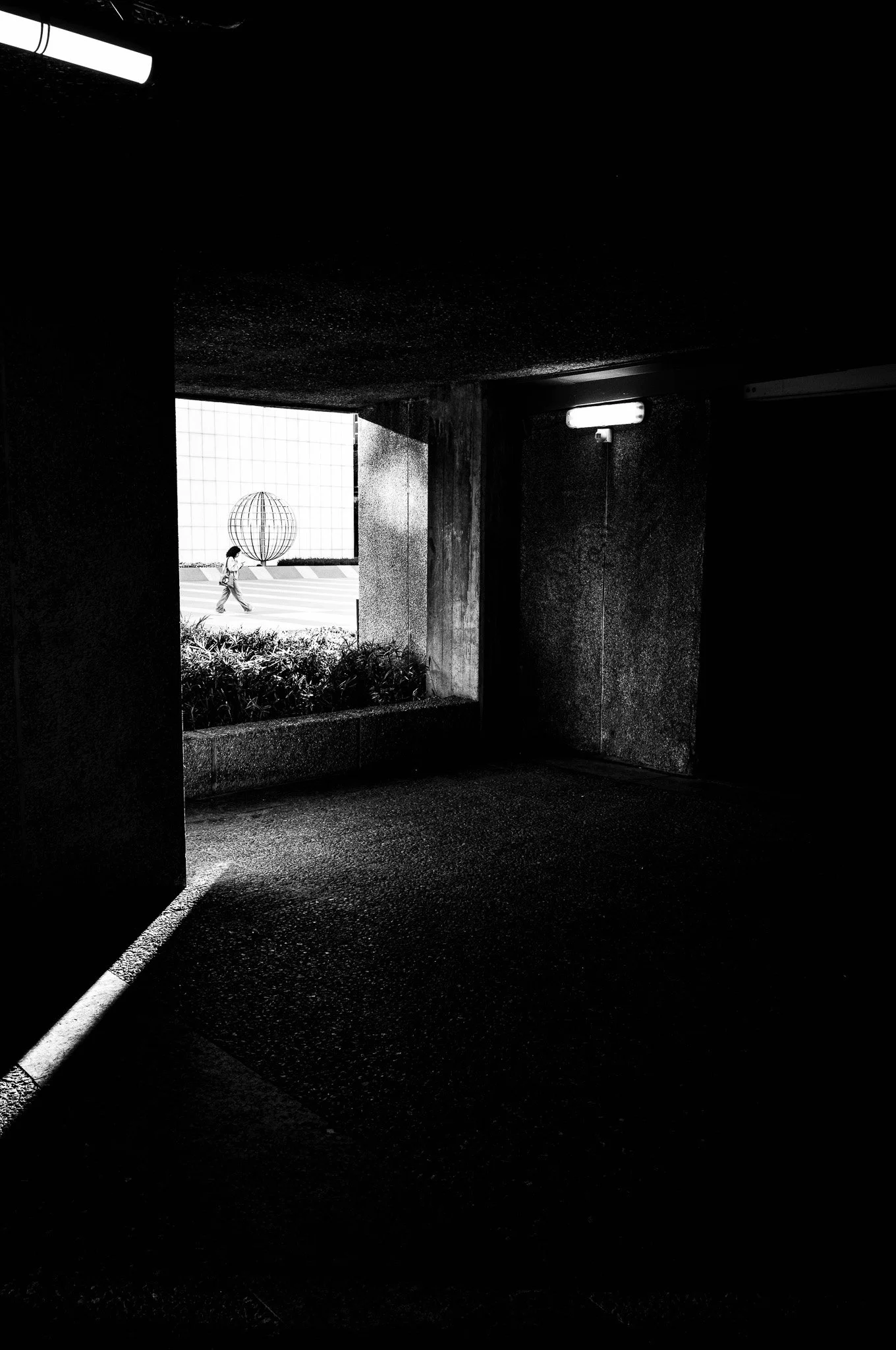 Vista desde un pasillo oscuro hacia la luz exterior, con un niño caminando por la calle y una estructura redonda en el fondo.