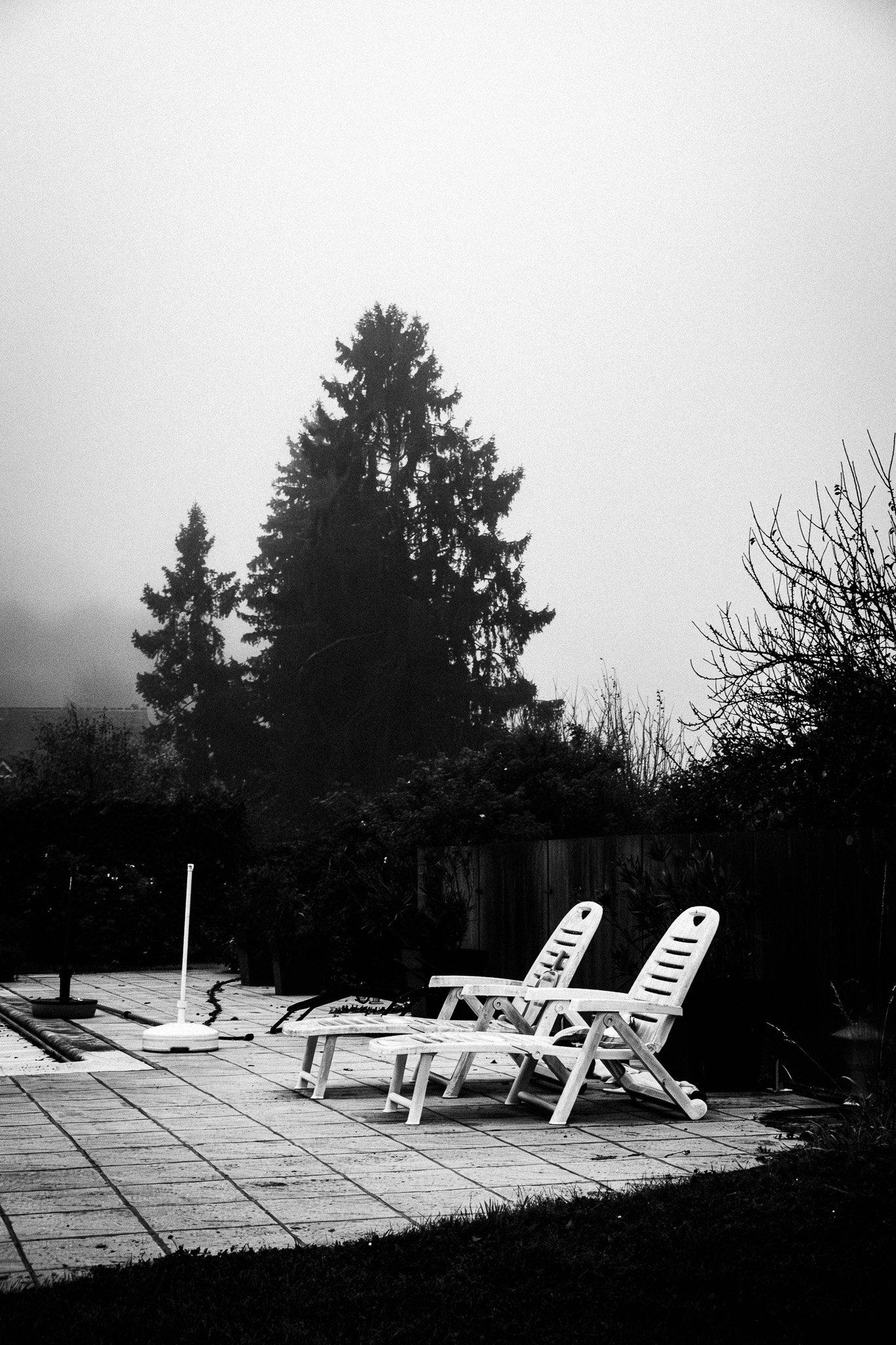 Dos sillas de jardín blancas en una terraza, con árboles y un cielo nublado en el fondo.