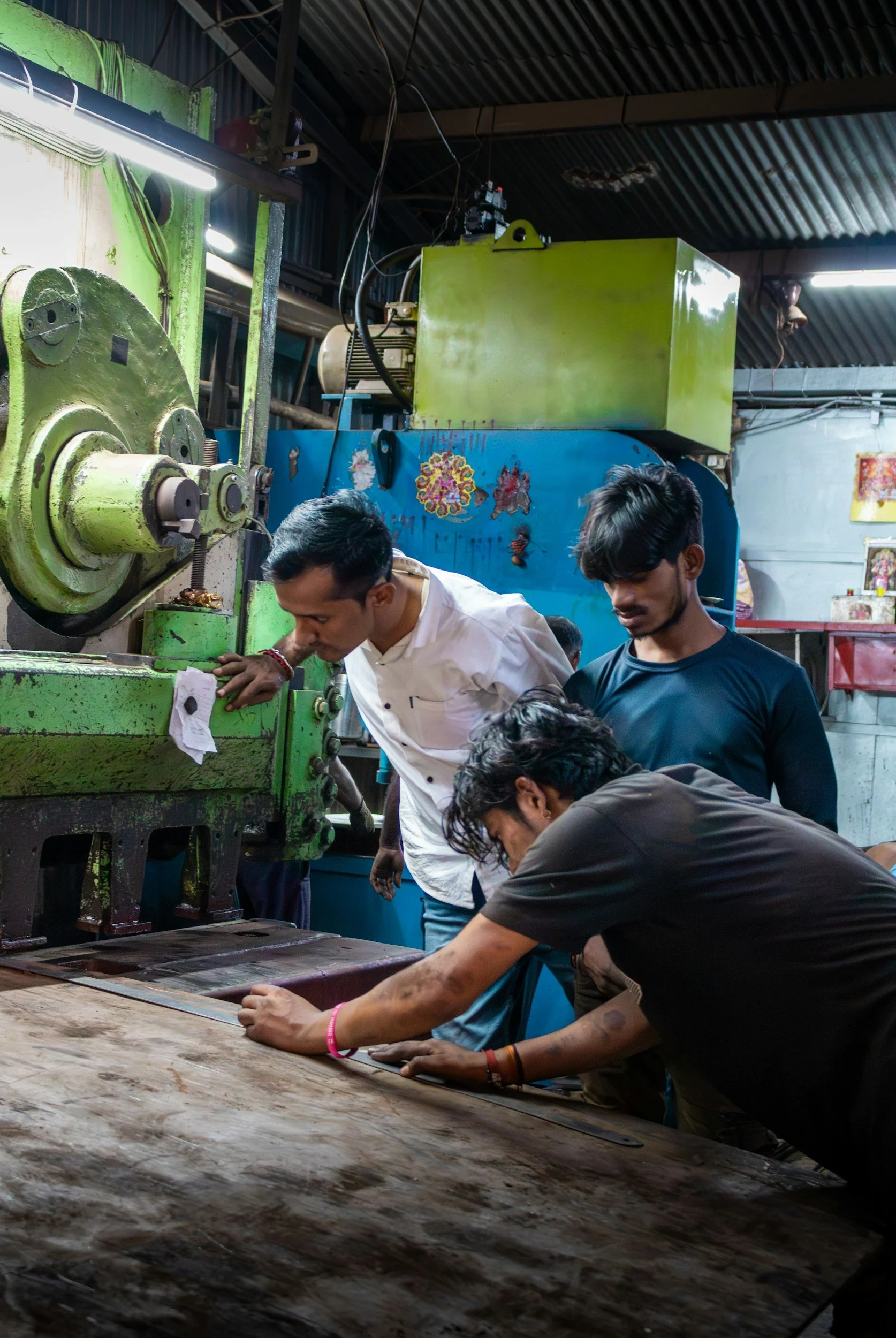 Four people working together on a large green machine in an industrial workshop with colorful decorations on the wall.