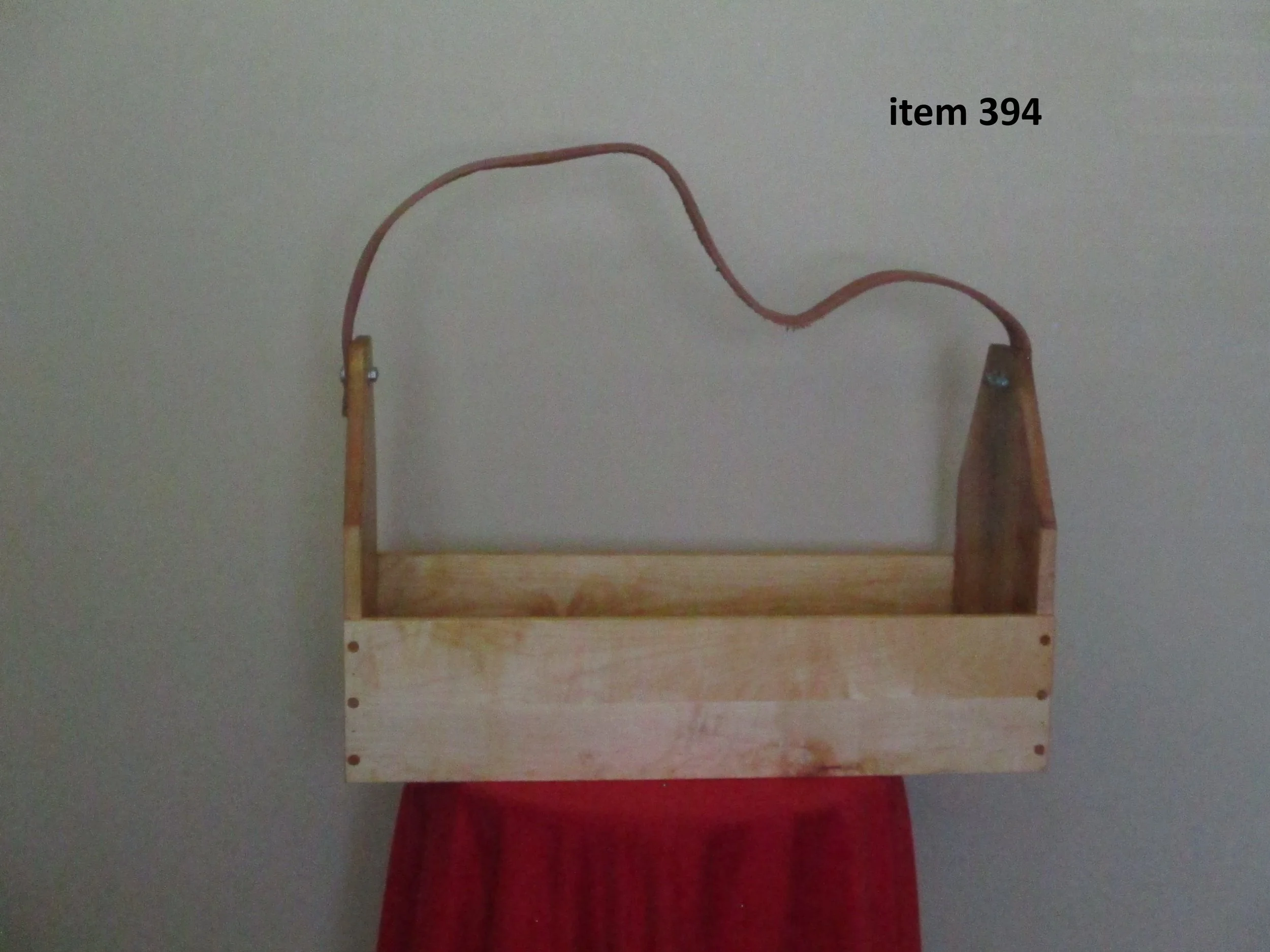 Empty wooden basket with a handle, hanging against a wall, with a red cloth underneath.