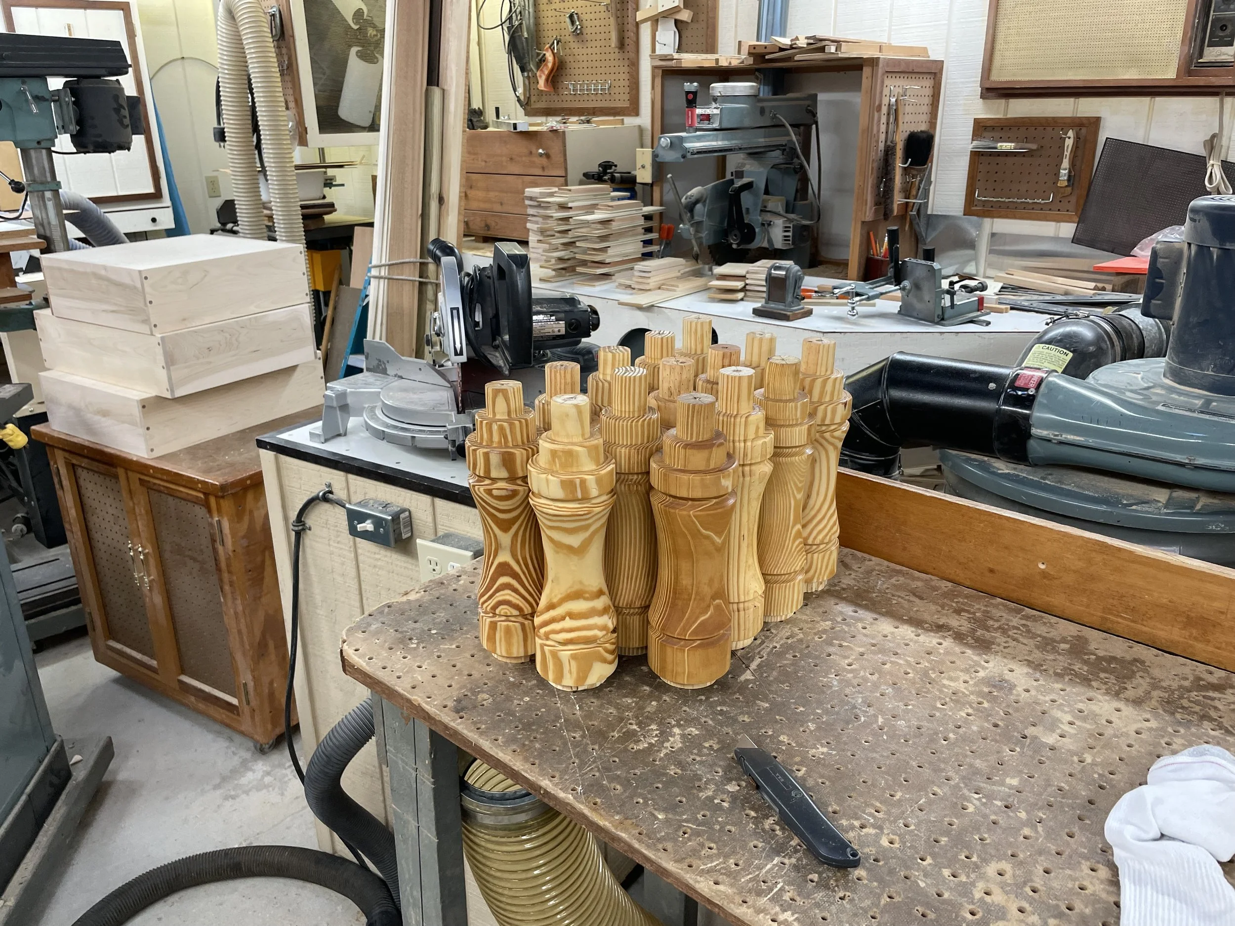 A woodworking workshop with wooden clamp handles arranged on a workbench, surrounded by woodworking tools, equipment, and wooden pieces.