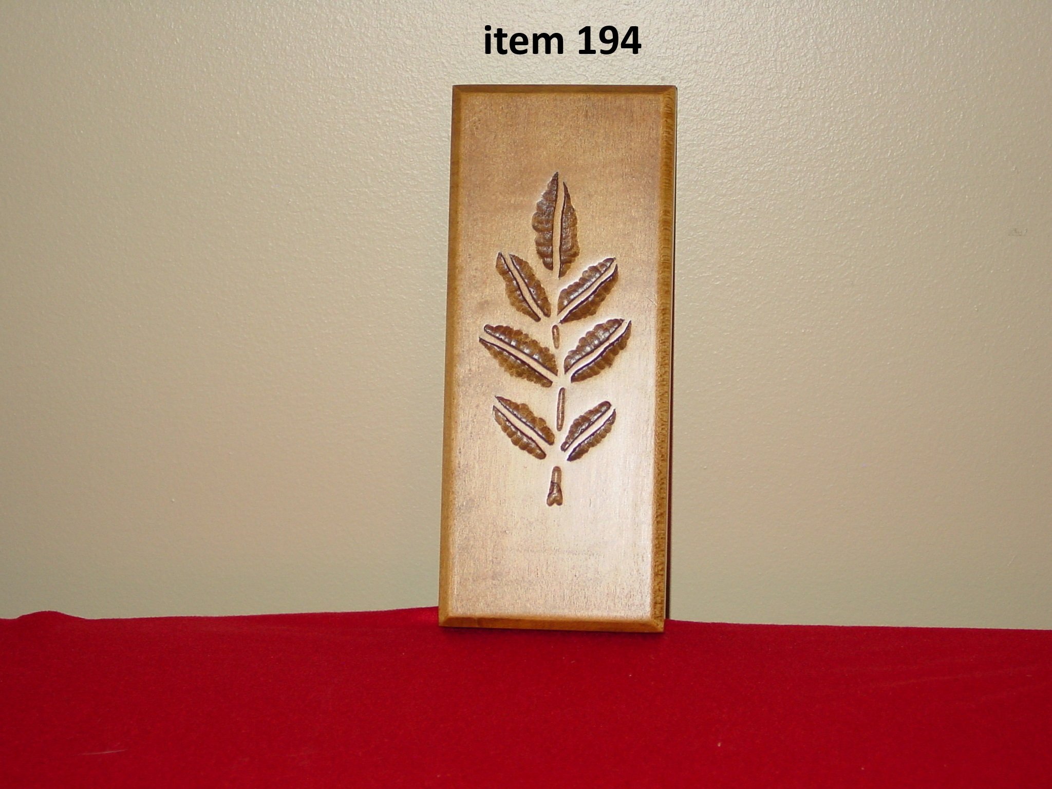 Wooden plaque with carved leaf design placed on a red surface against a beige wall, labeled 'item 194' at the top.
