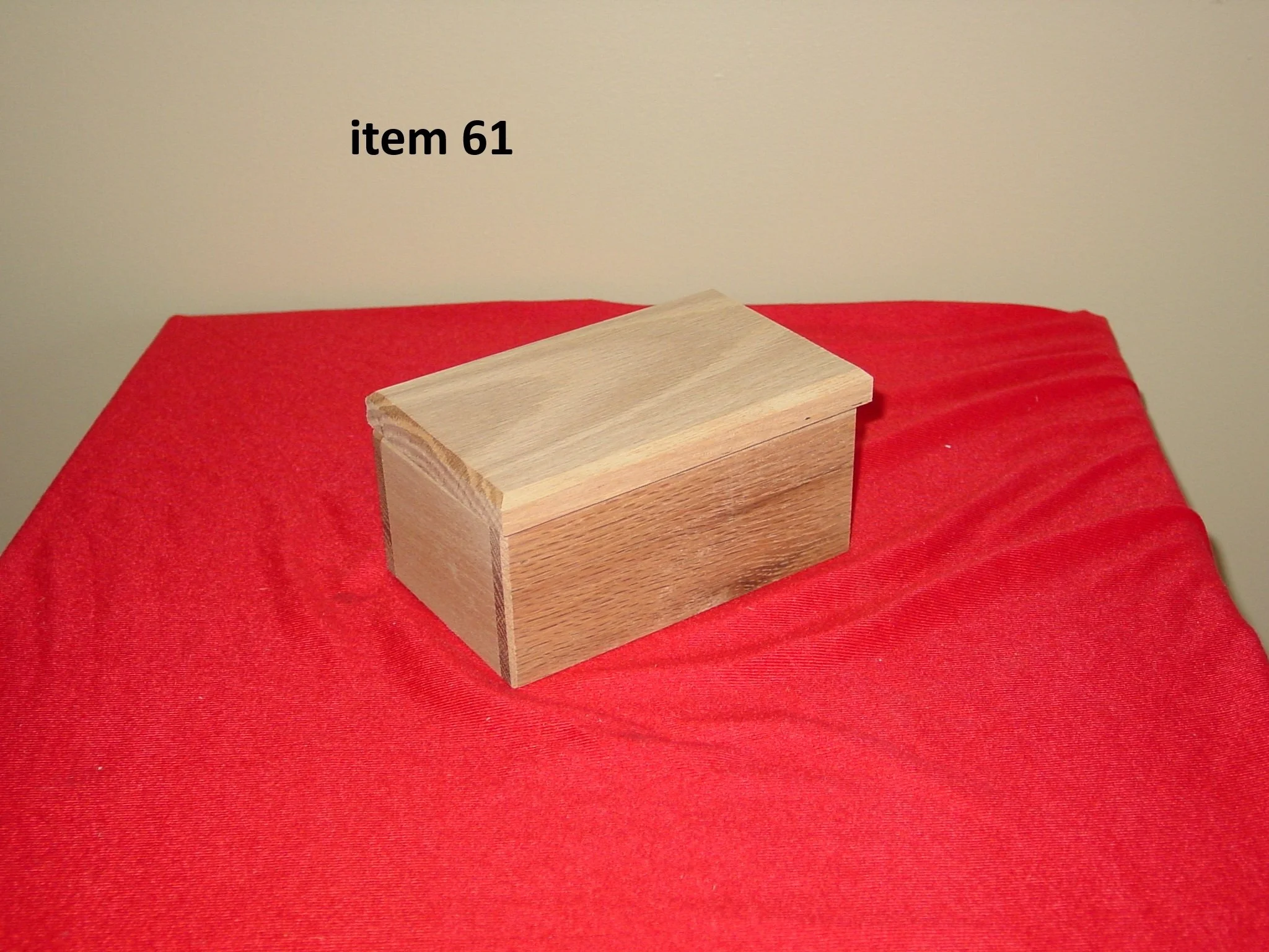 A small wooden box with a lid, placed on a red cloth, with the label 'item 61' in black text above it.
