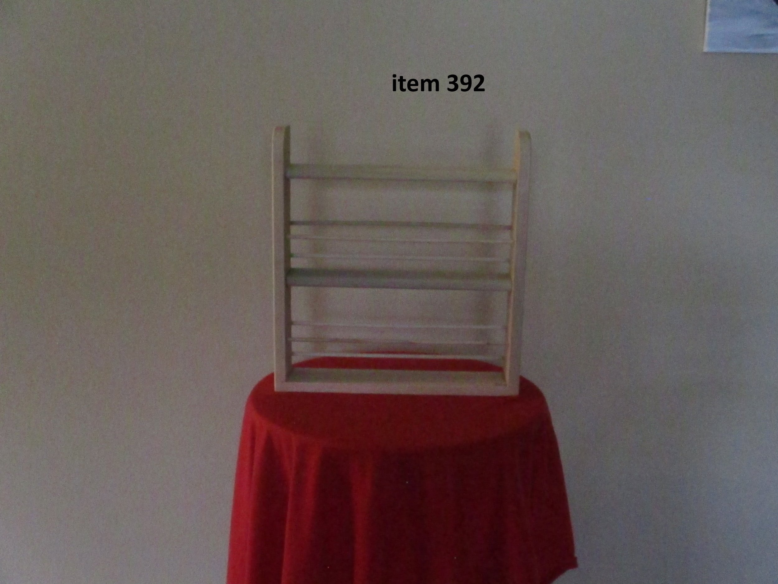Empty wooden dish rack with the label 'item 392' on a red-draped table against a plain wall.