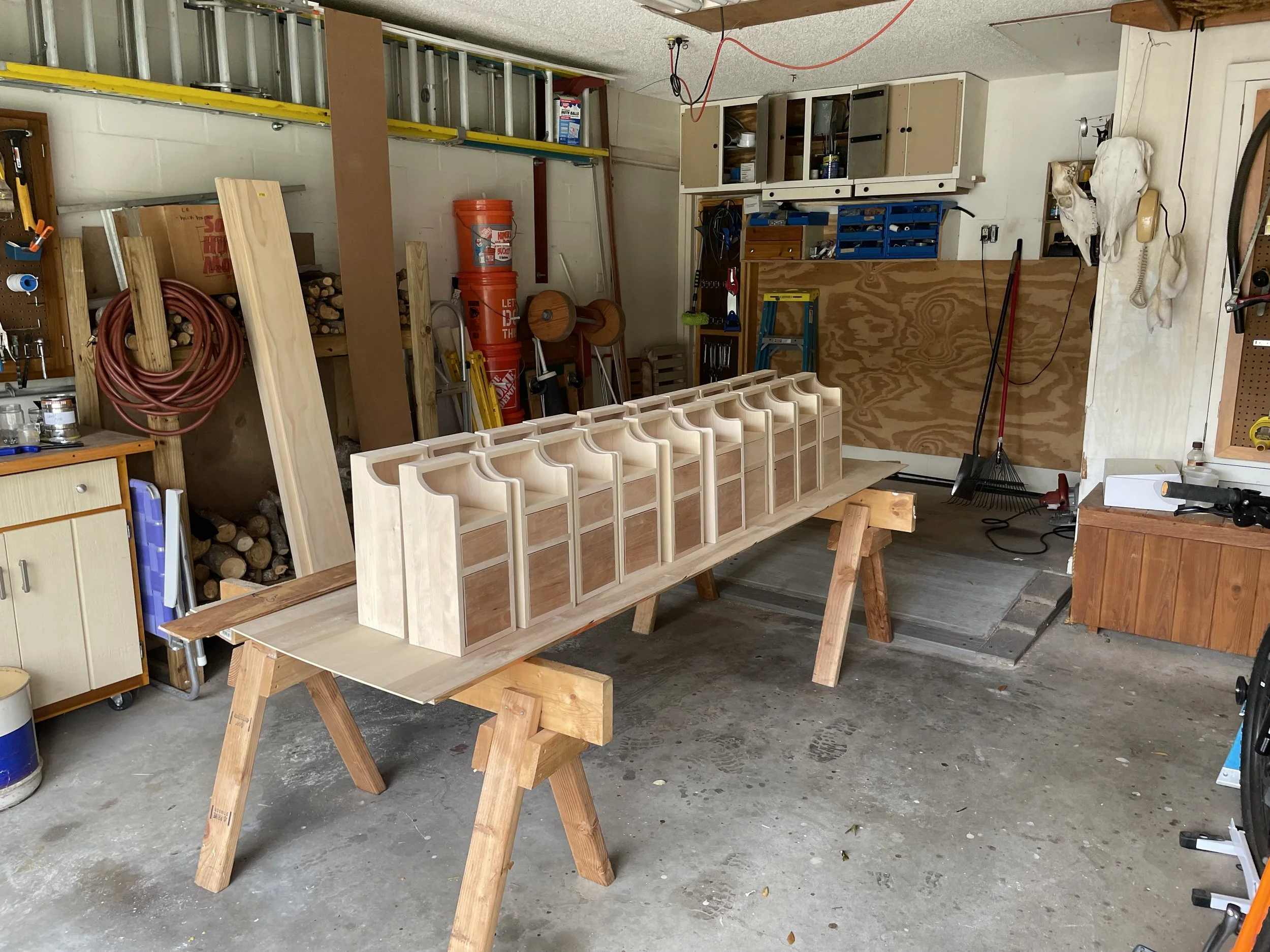 Wooden structure in progress in a garage workshop, supported by sawhorses, with various tools and storage shelves in the background.