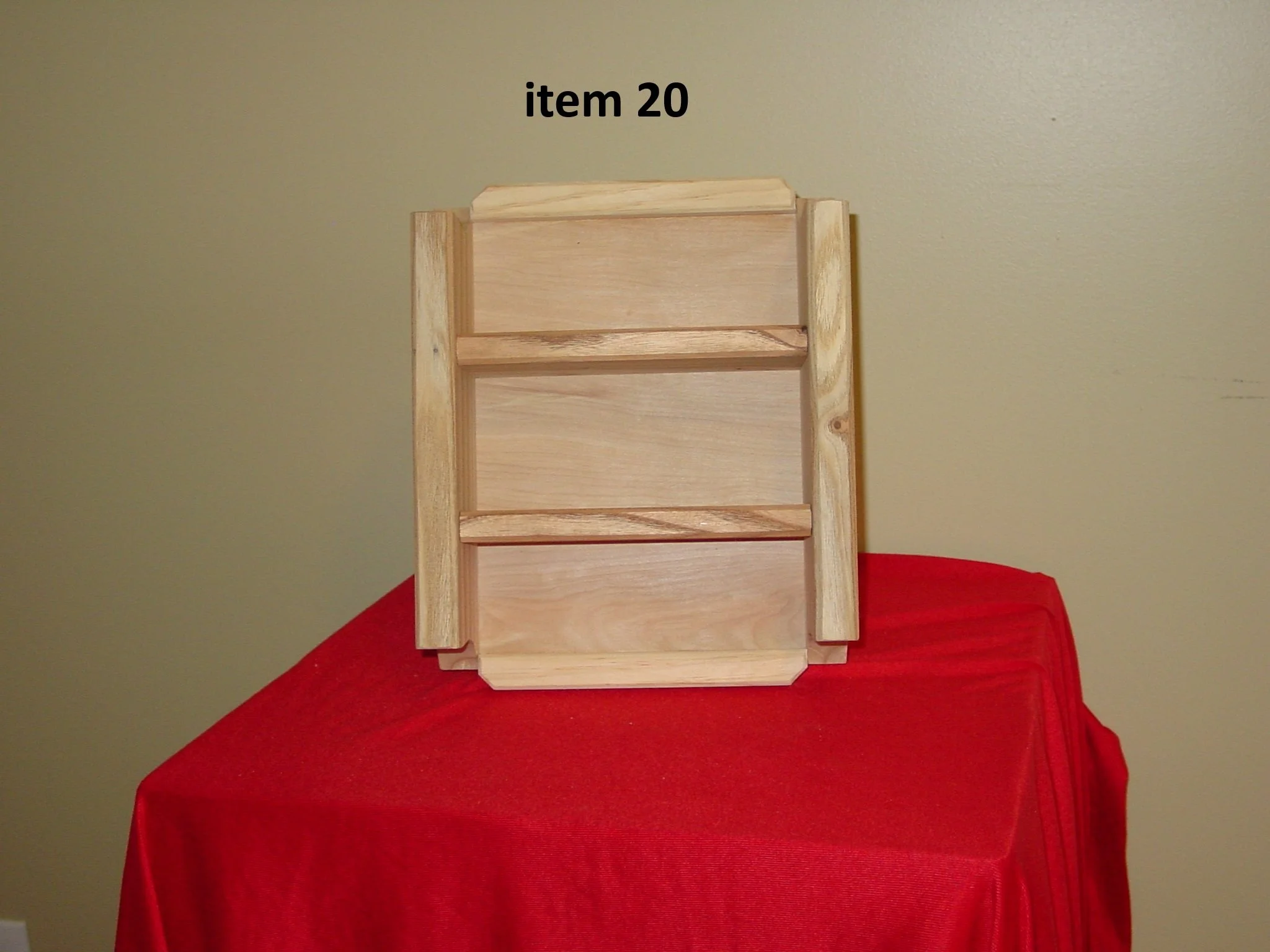 A wooden shelf with three compartments, placed on a red cloth-covered surface against a plain wall, labeled as item 20.