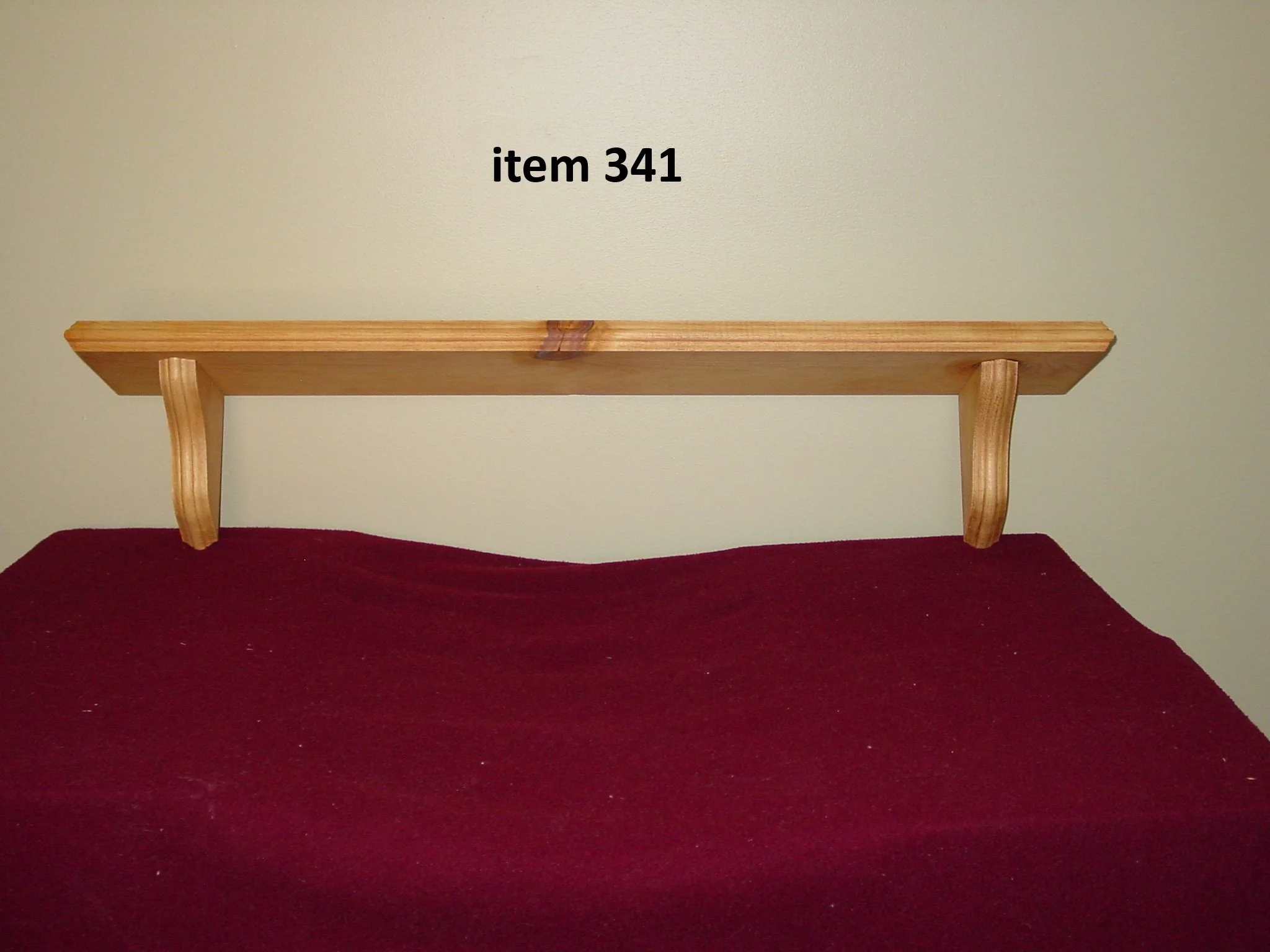 Wooden shelf with two brackets mounted on a beige wall above a red fabric surface, labeled 'item 341'.